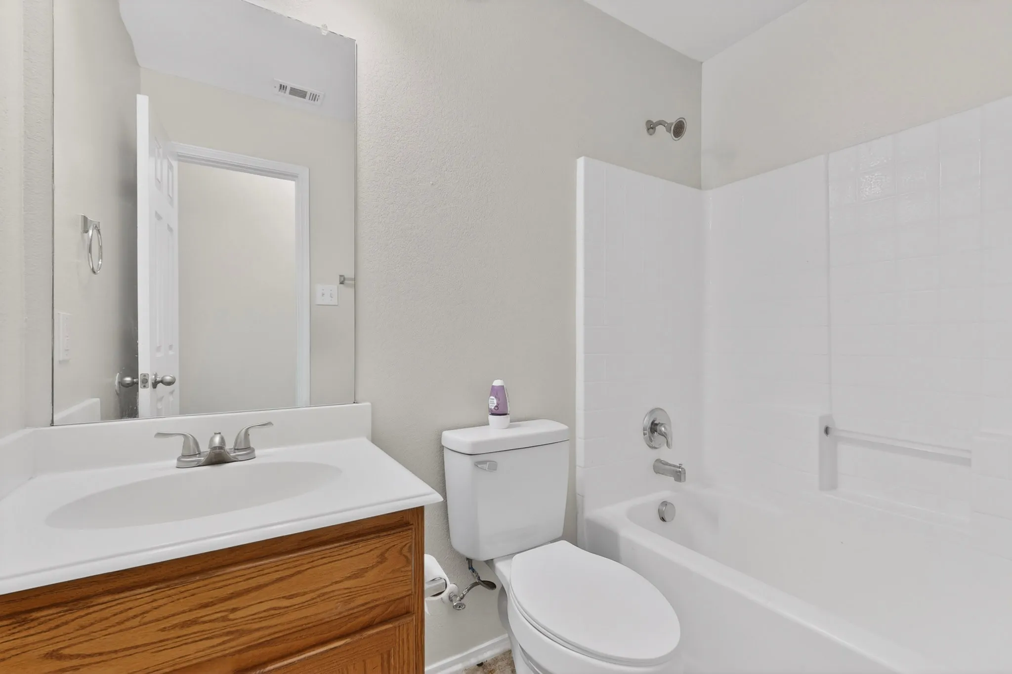Bathroom featuring a wood-finish vanity, white countertop with integrated sink, chrome faucet, toilet, and a bathtub with white tile surround