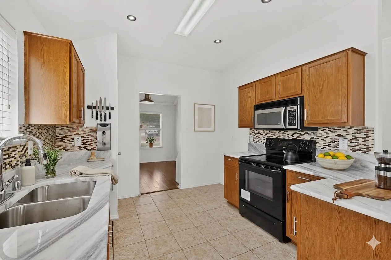 Kitchen featuring wood cabinetry, white countertops, stainless steel double basin sink, black appliances, and a tiled backsplash