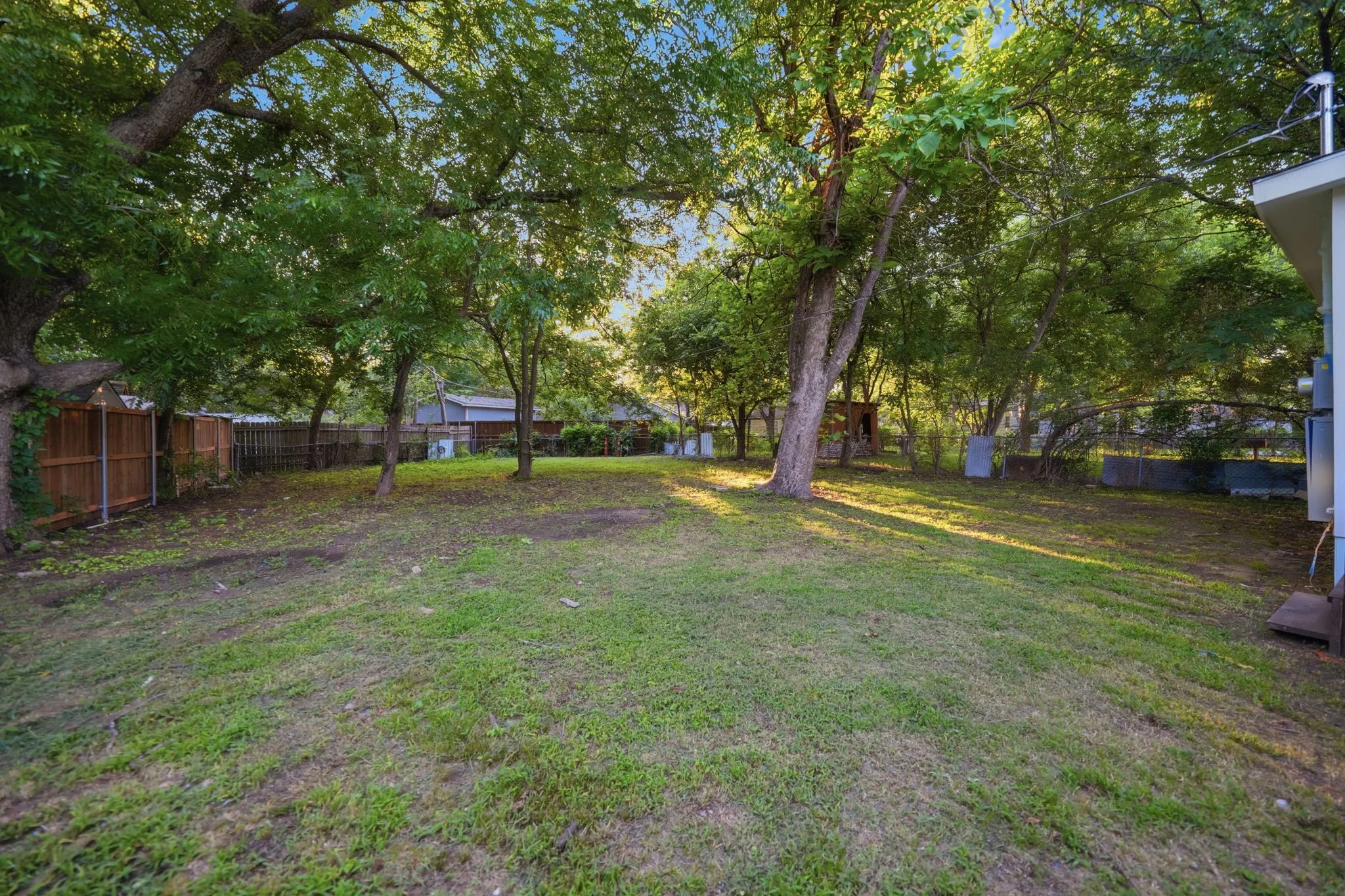 Expansive grassy yard featuring mature trees and partial wood fencing