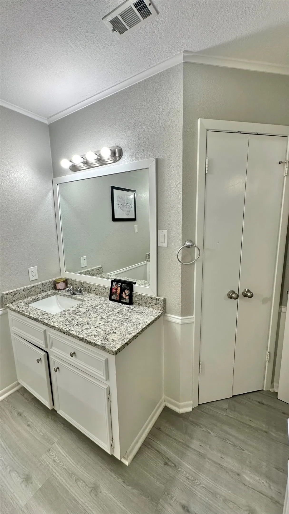 Bathroom featuring a white vanity with a light-toned speckled granite countertop, an undermount sink, and a framed mirror with overhead lighting