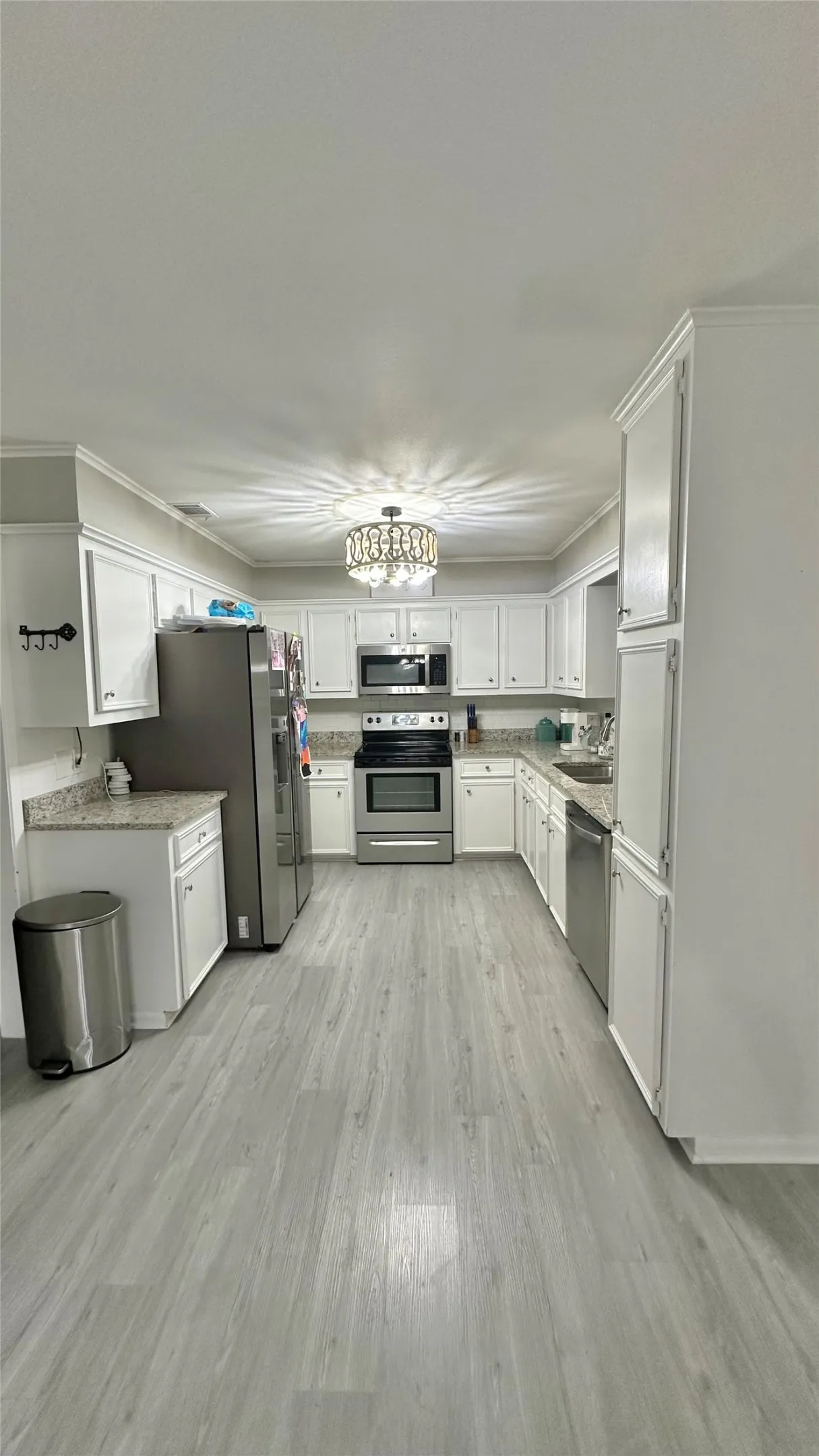 Kitchen featuring vinyl plank flooring, white cabinetry, granite countertops, stainless steel appliances, and a decorative ceiling light fixture