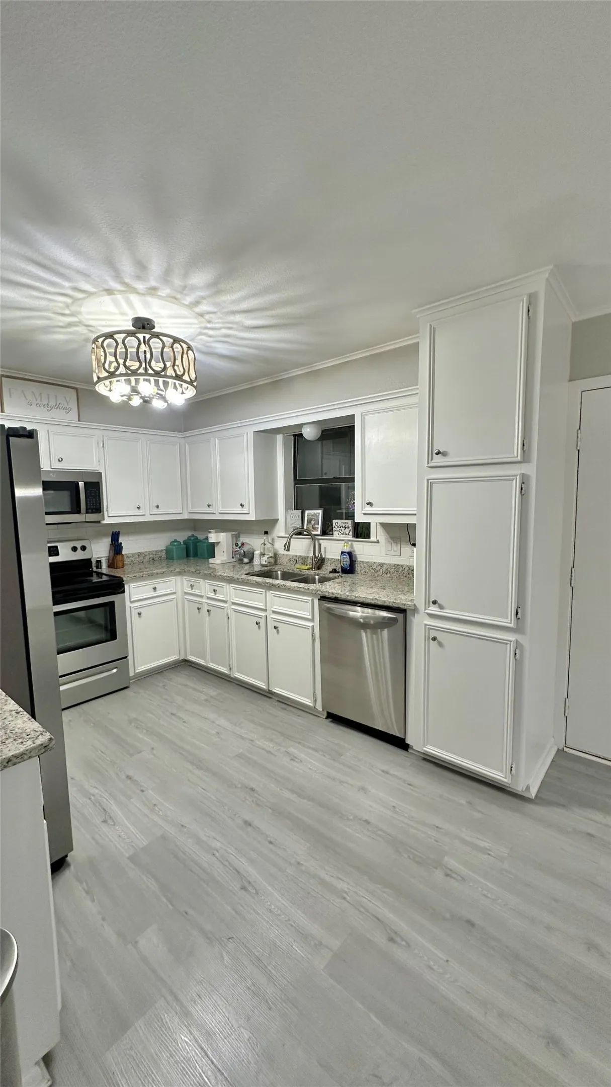 Kitchen featuring white shaker-style cabinetry, light-toned, stainless steel appliances, granite countertops, and a decorative ceiling light fixture