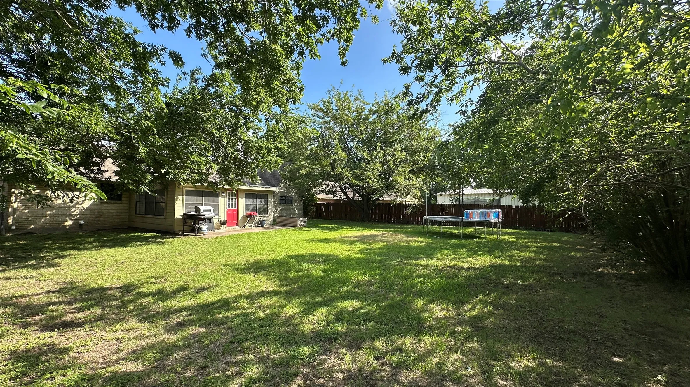 Expansive backyard featuring a lush lawn, mature trees, and a concrete patio