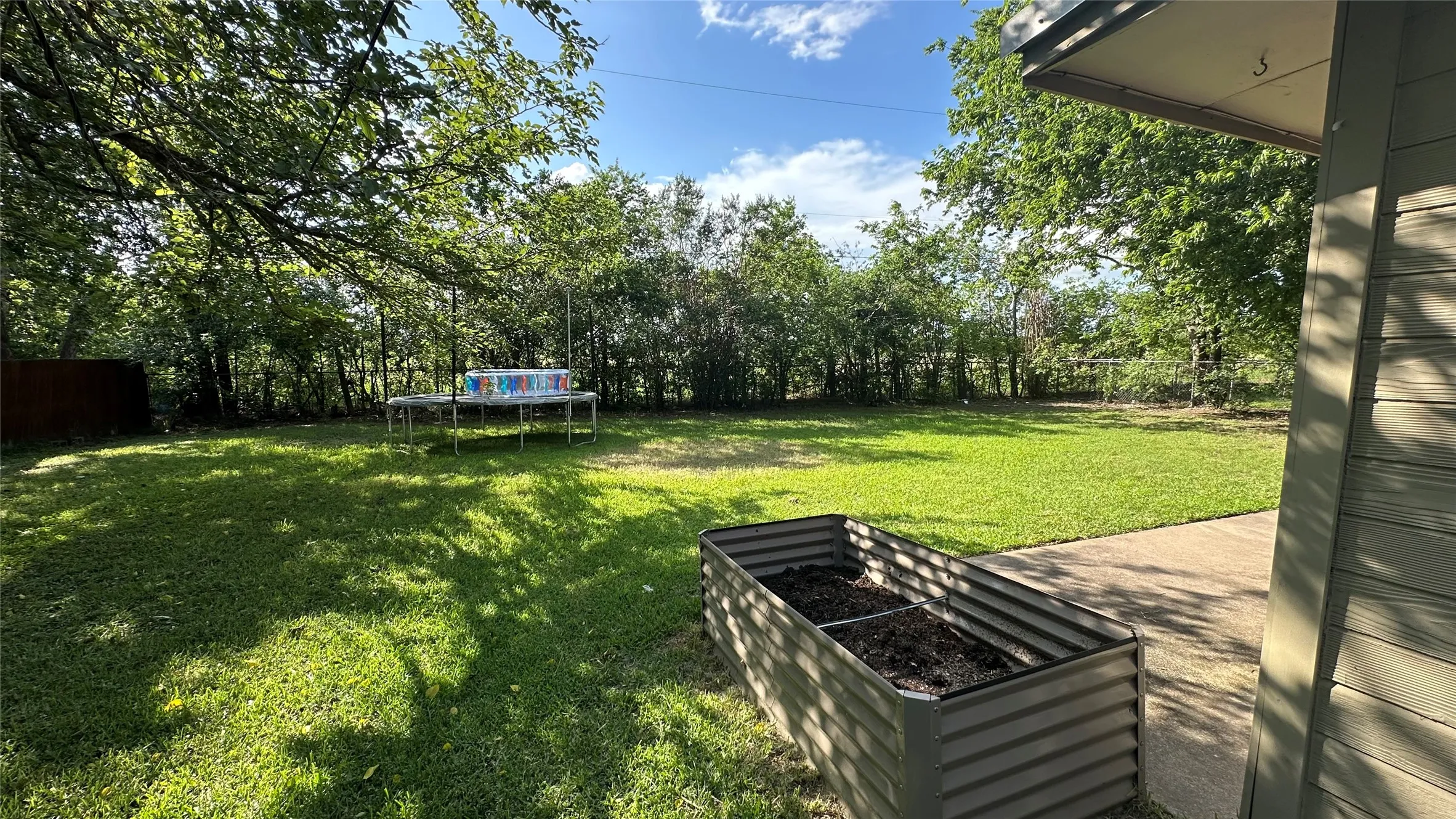 Expansive yard featuring a manicured lawn, established shade trees, and a concrete patio