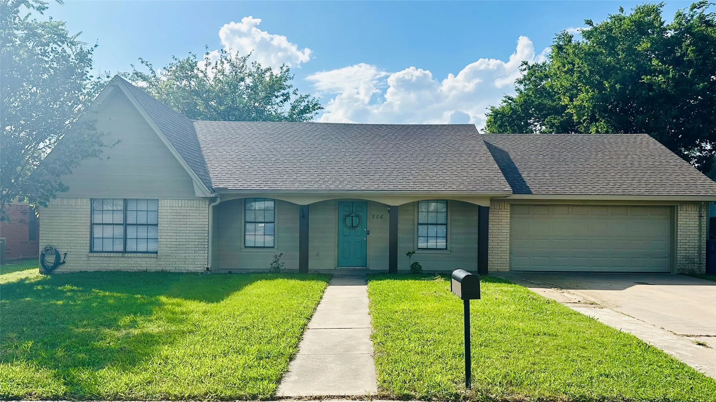 Single-story residence featuring a brick facade and siding, a covered front porch with decorative columns, a teal entry door, and a two-car attached garage