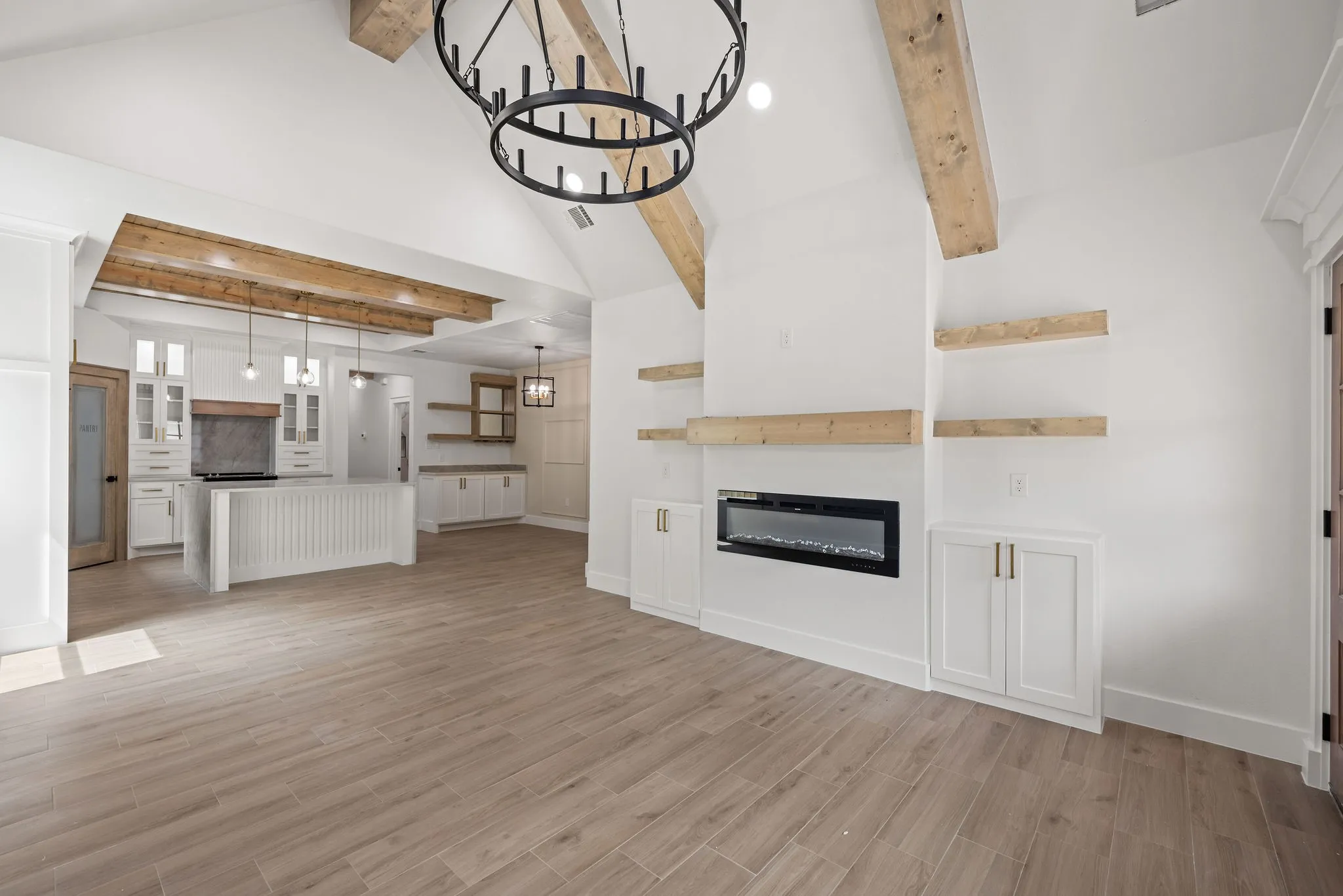 Vaulted ceiling with exposed wood beams, wood-finish flooring, built-in electric fireplace, recessed lighting, and a kitchen featuring a center island with pendant lighting