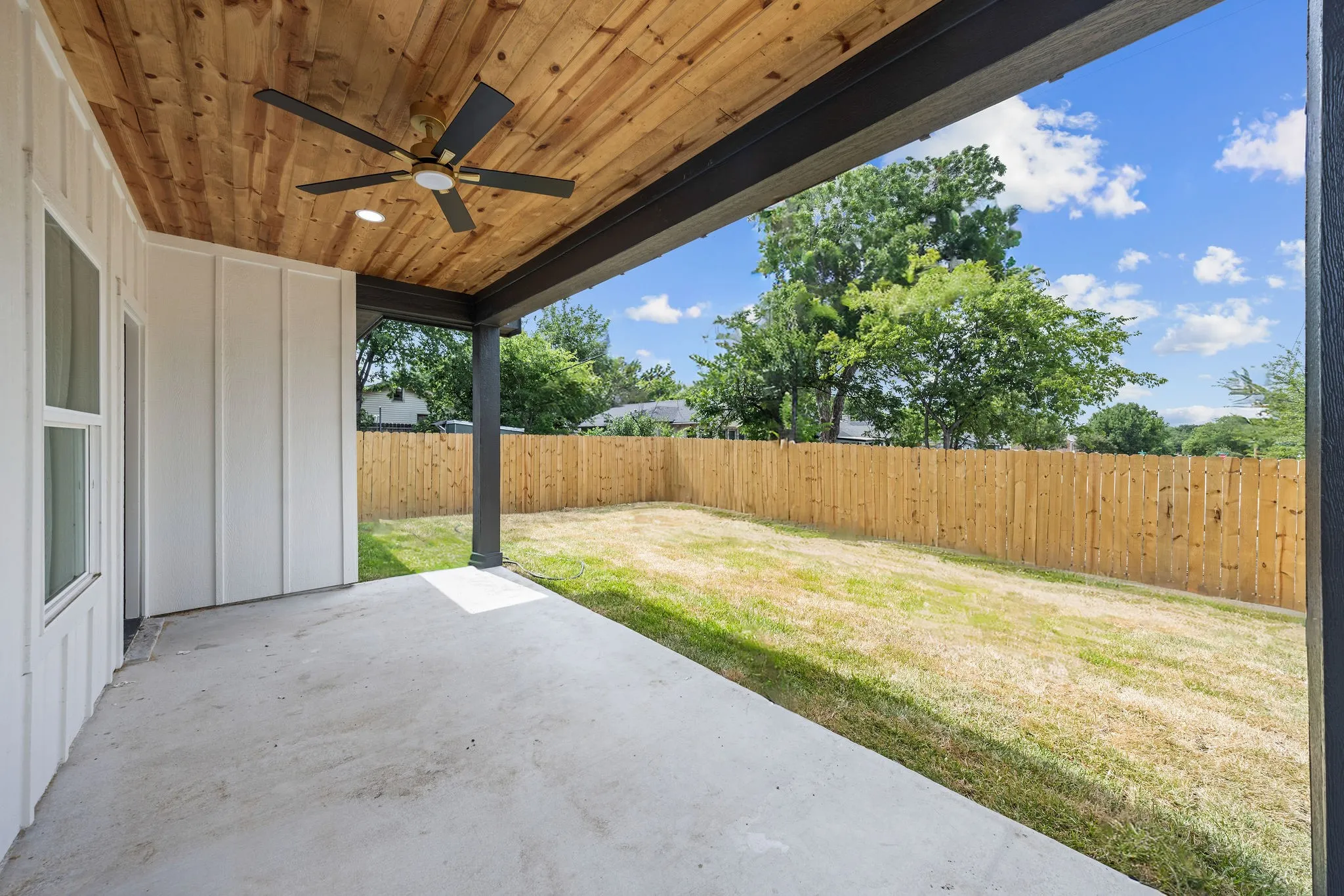 Covered concrete patio with wood-panel ceiling, featuring a ceiling fan and recessed lighting
