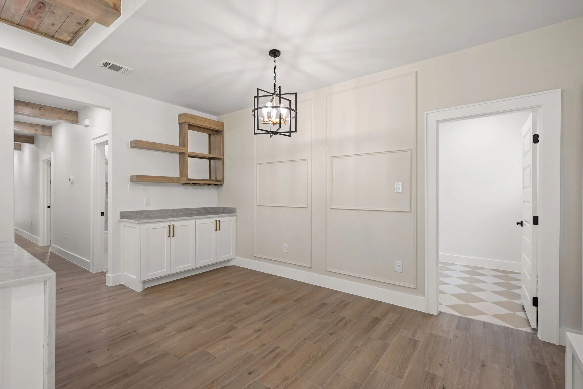 Open-concept living area featuring wood-finish flooring, a built-in dry bar with wood shelving and lower cabinetry, and a geometric chandelier