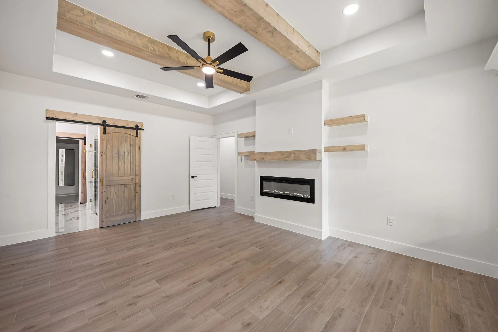 Spacious interior with wood-finish flooring and a tray ceiling featuring exposed wood beams and recessed lighting