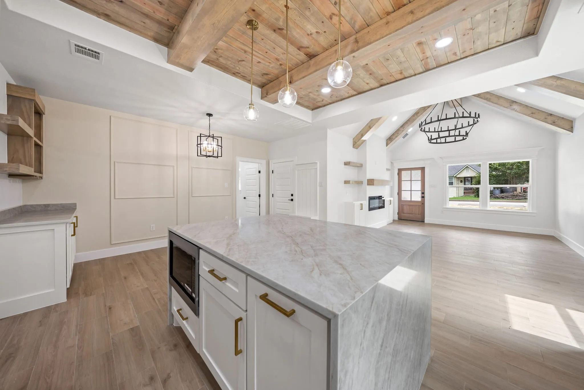 Spacious open-concept interior featuring a substantial kitchen island with a built-in microwave, wood-finish flooring, and a vaulted ceiling with exposed wood beams