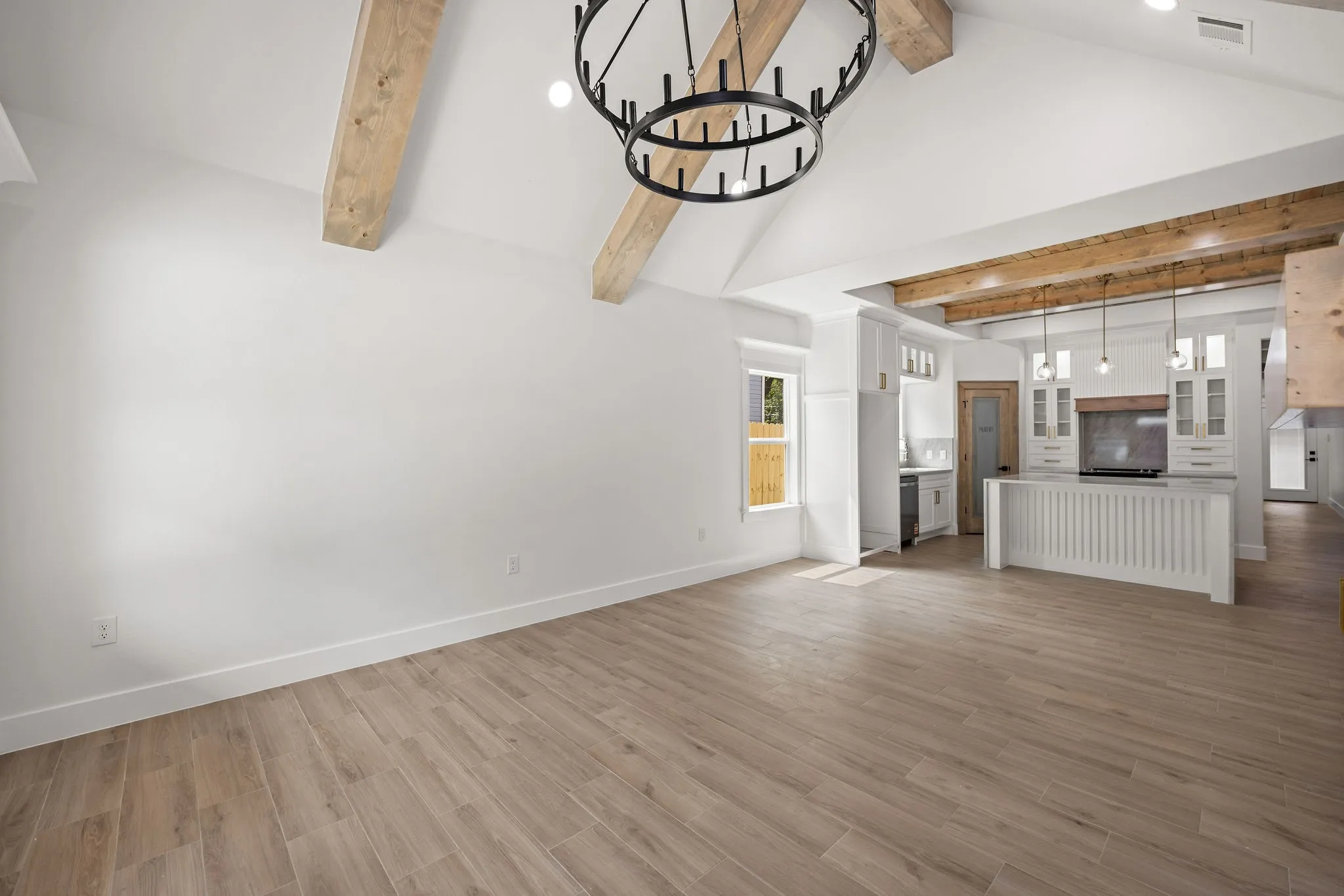 Spacious open-concept living area featuring a vaulted ceiling with exposed wood beams and a large circular chandelier