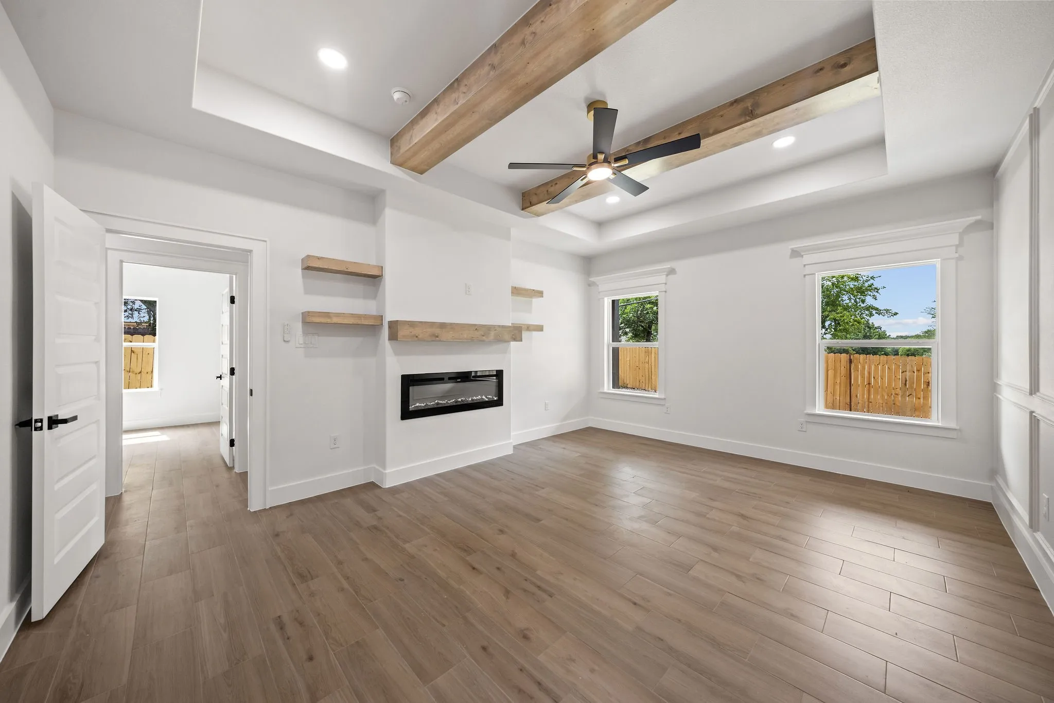 Spacious room featuring wood-finish flooring, a tray ceiling with exposed wood beams, and a modern ceiling fan
