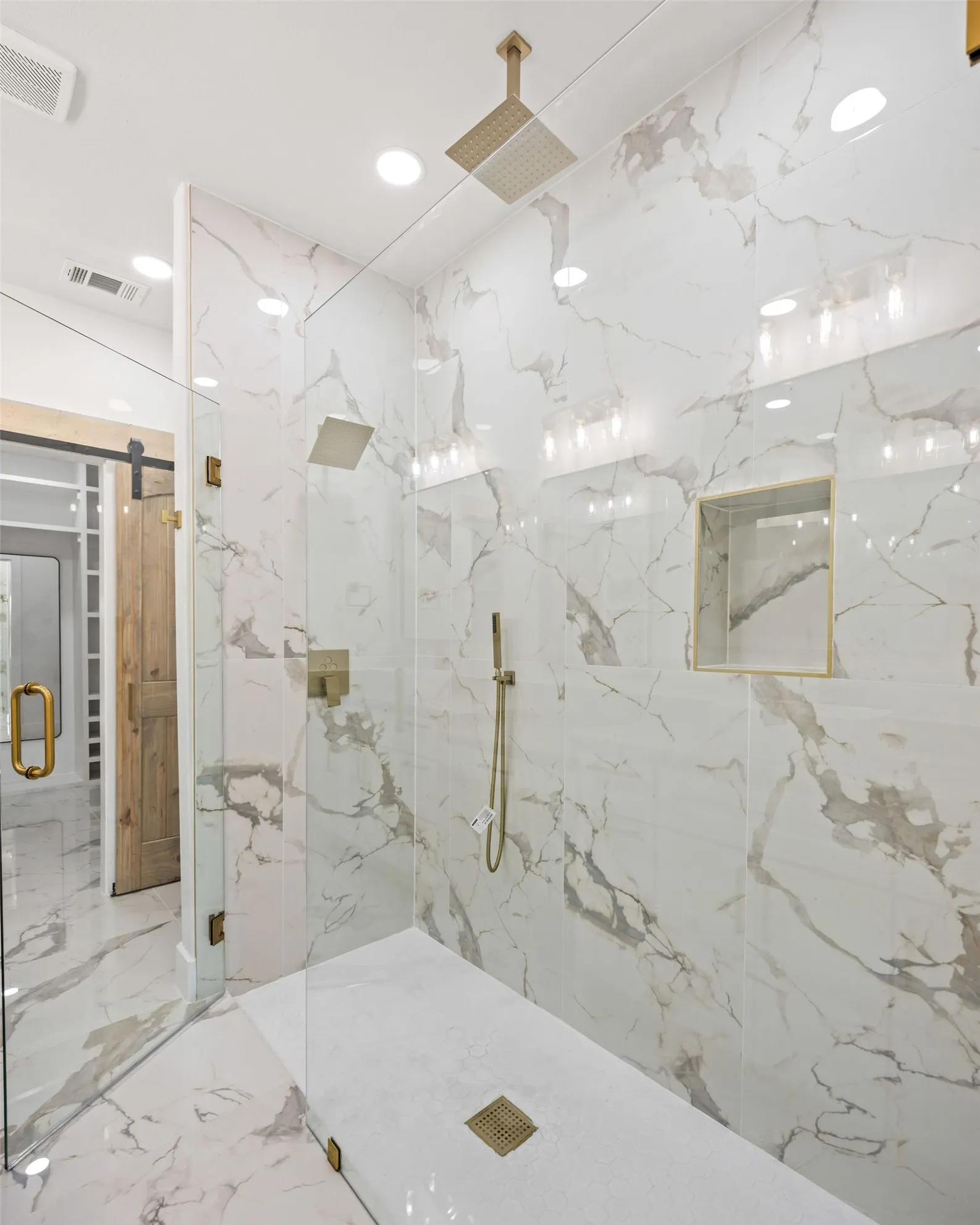 Glass-enclosed shower with full-height marbled wall tiling, square rain shower head, hand-held shower fixture, built-in niche, and gold-toned hardware