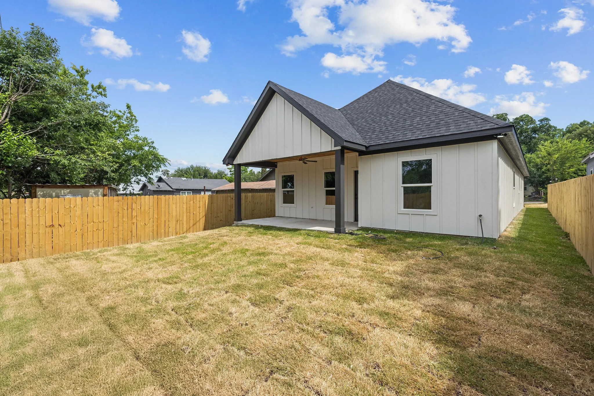 Spacious backyard featuring a full wood privacy fence, covered patio with a ceiling fan, and modern siding