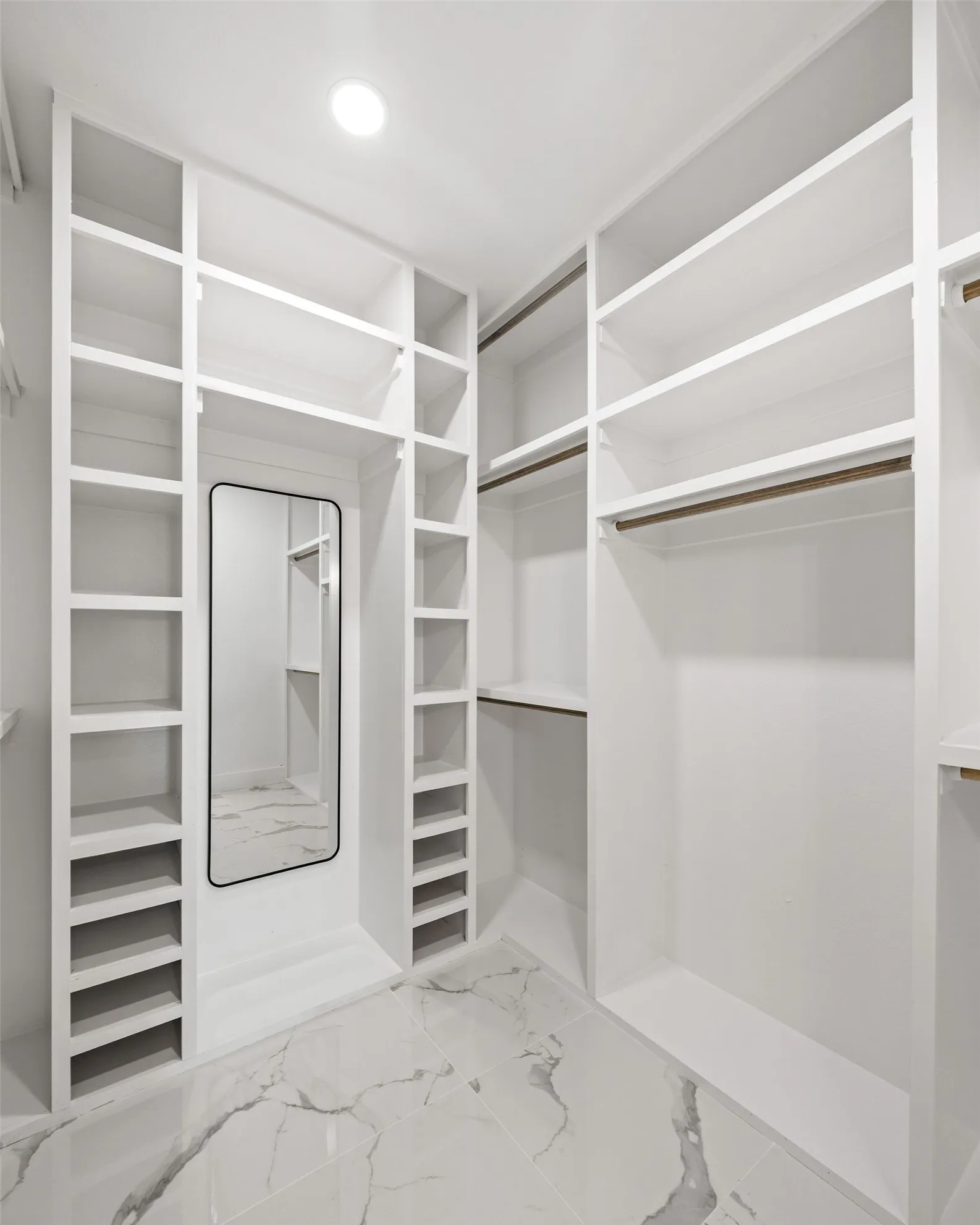 Custom-built closet featuring extensive white shelving, multiple hanging rods, dedicated shoe storage, and a full-length mirror