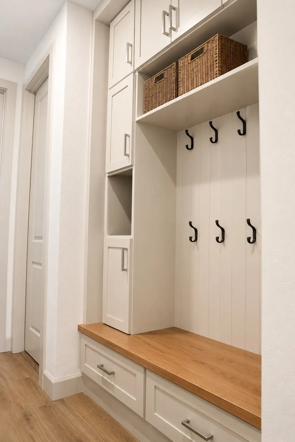 Built-in mudroom organization featuring a wood-finish bench, cabinetry with brushed nickel hardware, open shelving, and black coat hooks