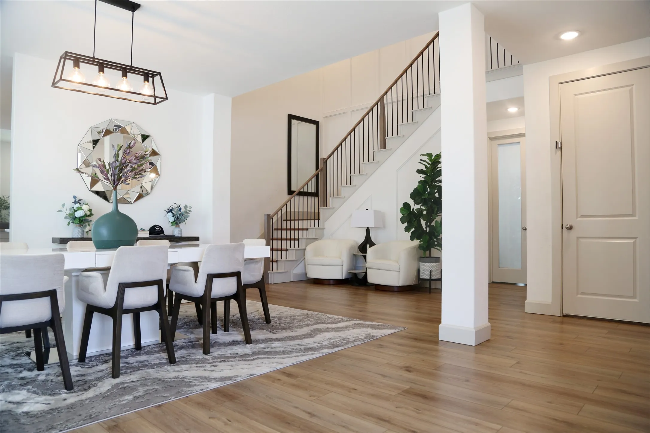 Open-concept interior featuring wood-finish flooring, a contemporary linear chandelier, a modern staircase with dark wood railings, and a panel door