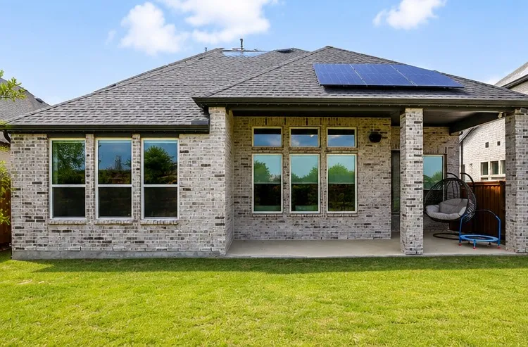 Rear exterior featuring a covered patio, brick construction, multiple windows, and a shingled roof with solar panels