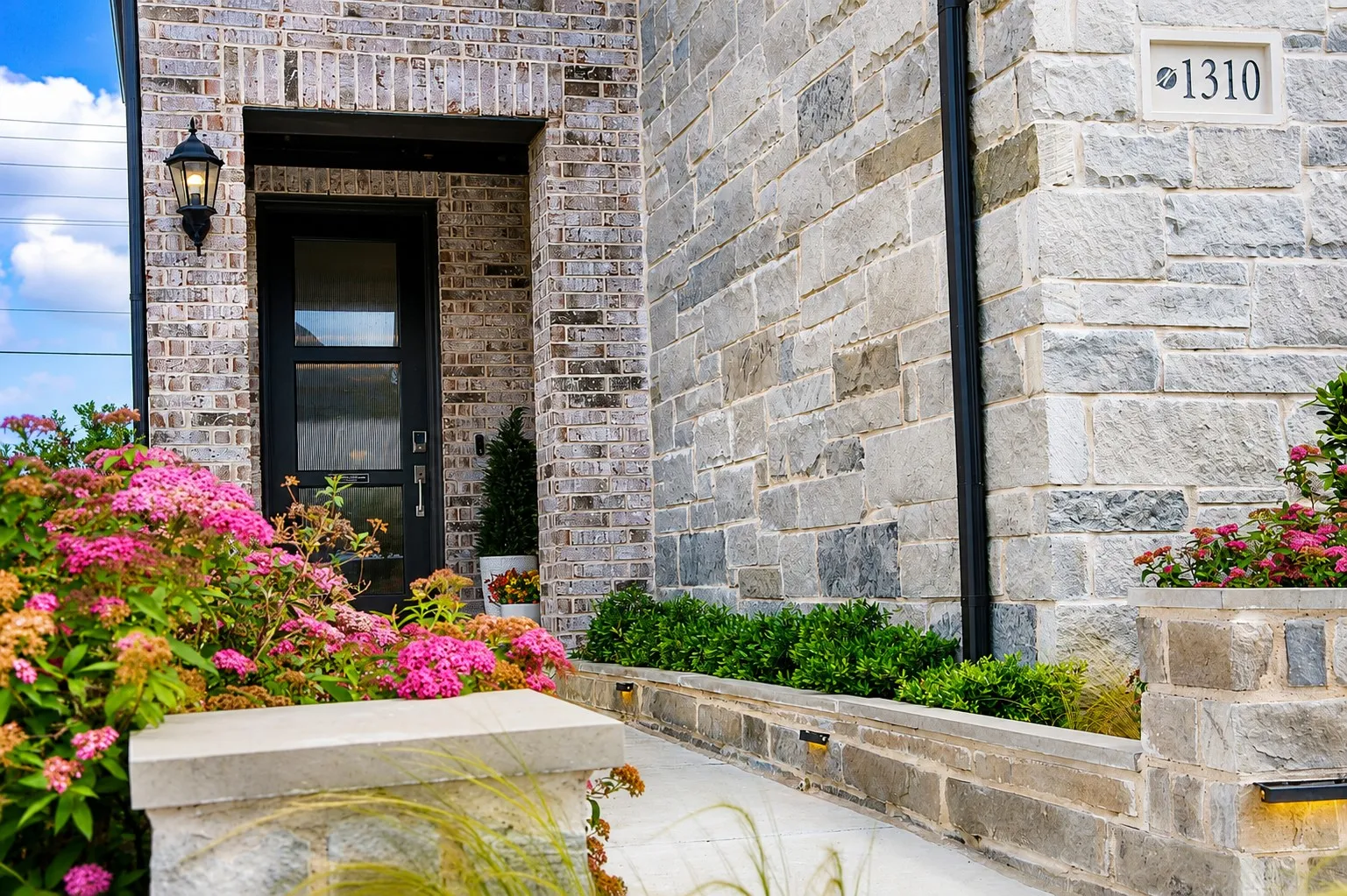 Brick and stone facade featuring a modern black entry door with frosted glass panels