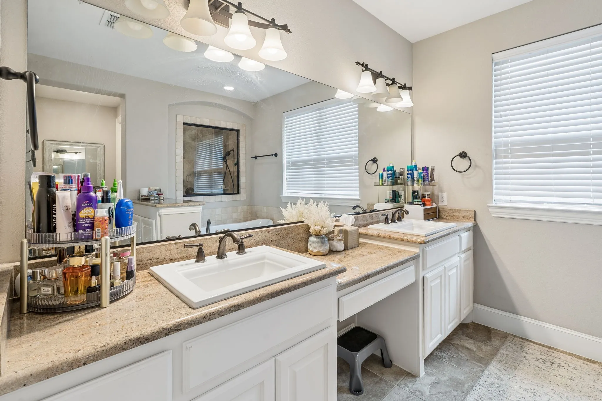 Bathroom vanity featuring dual sinks with bronze-finish fixtures, a full-width mirror, and a built-in makeup vanity space