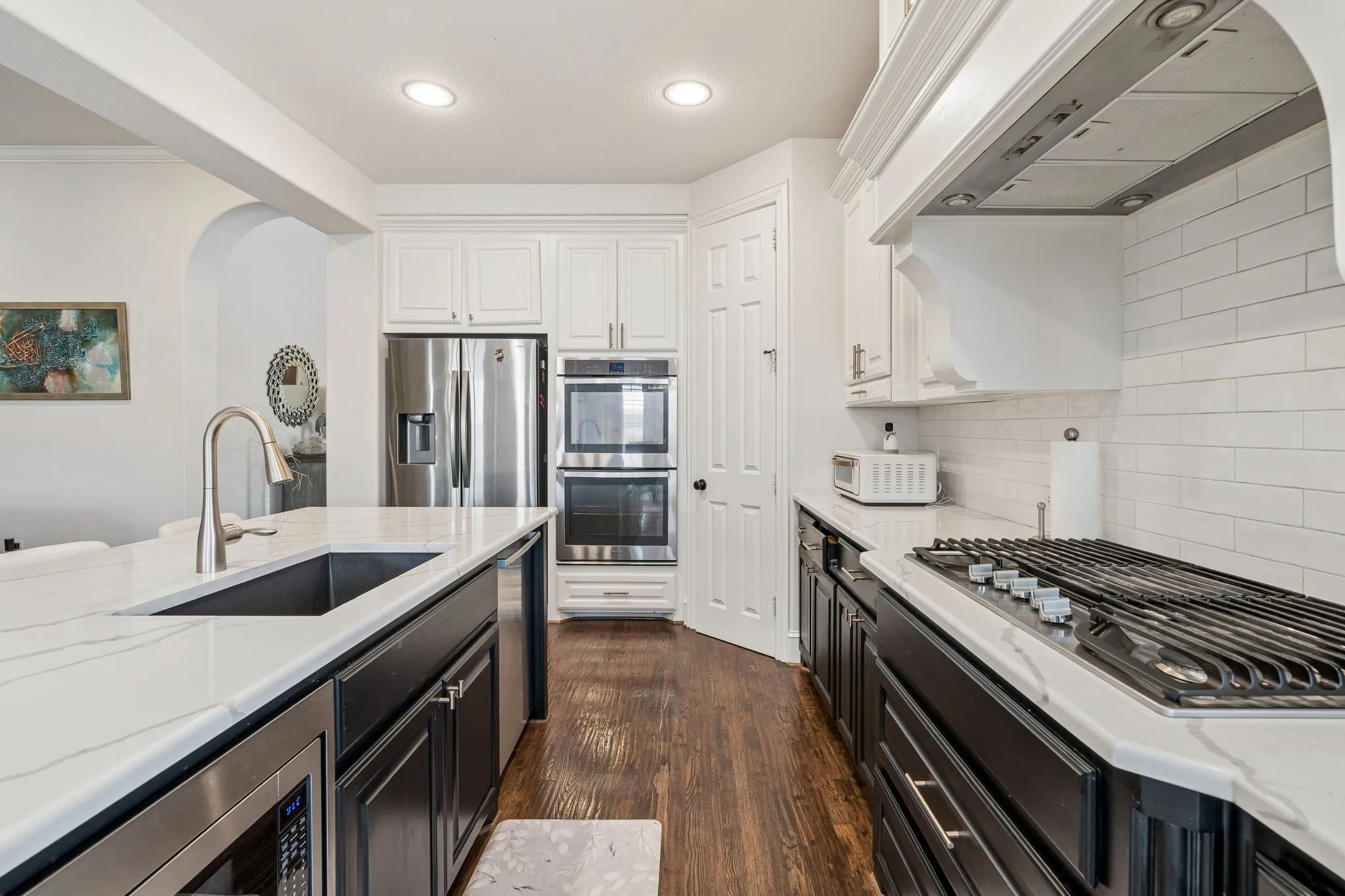 Kitchen featuring white countertops, dark wood-finish flooring, a built-in microwave, a gas cooktop with an overhead range hood, and stainless steel appliances