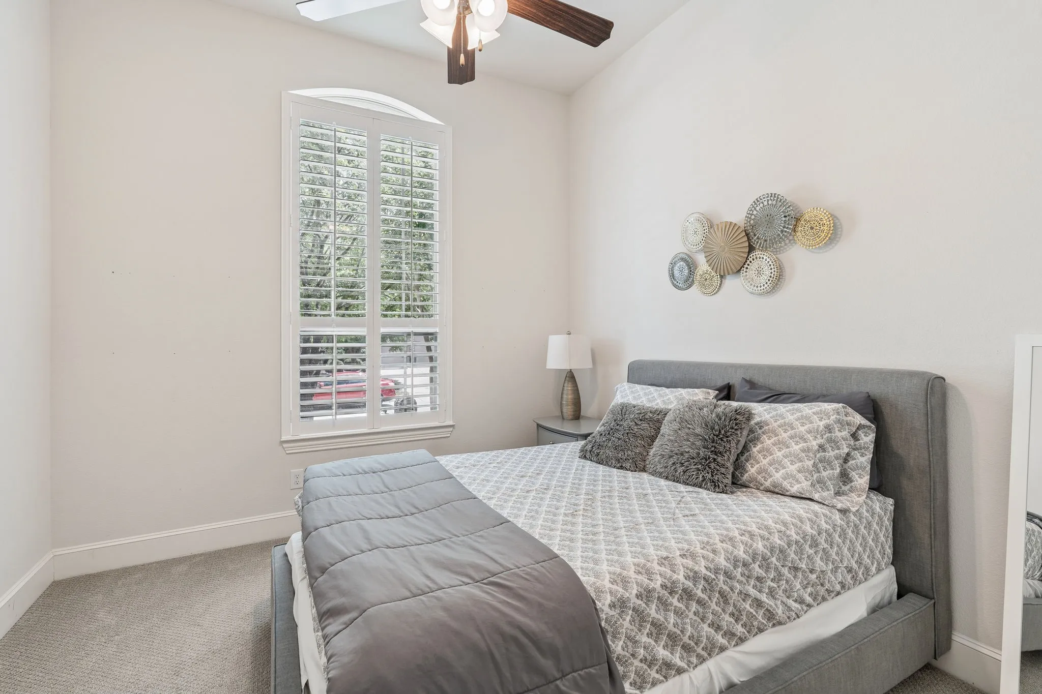 Arched window with plantation shutters, light neutral wall paint, and grey carpet flooring