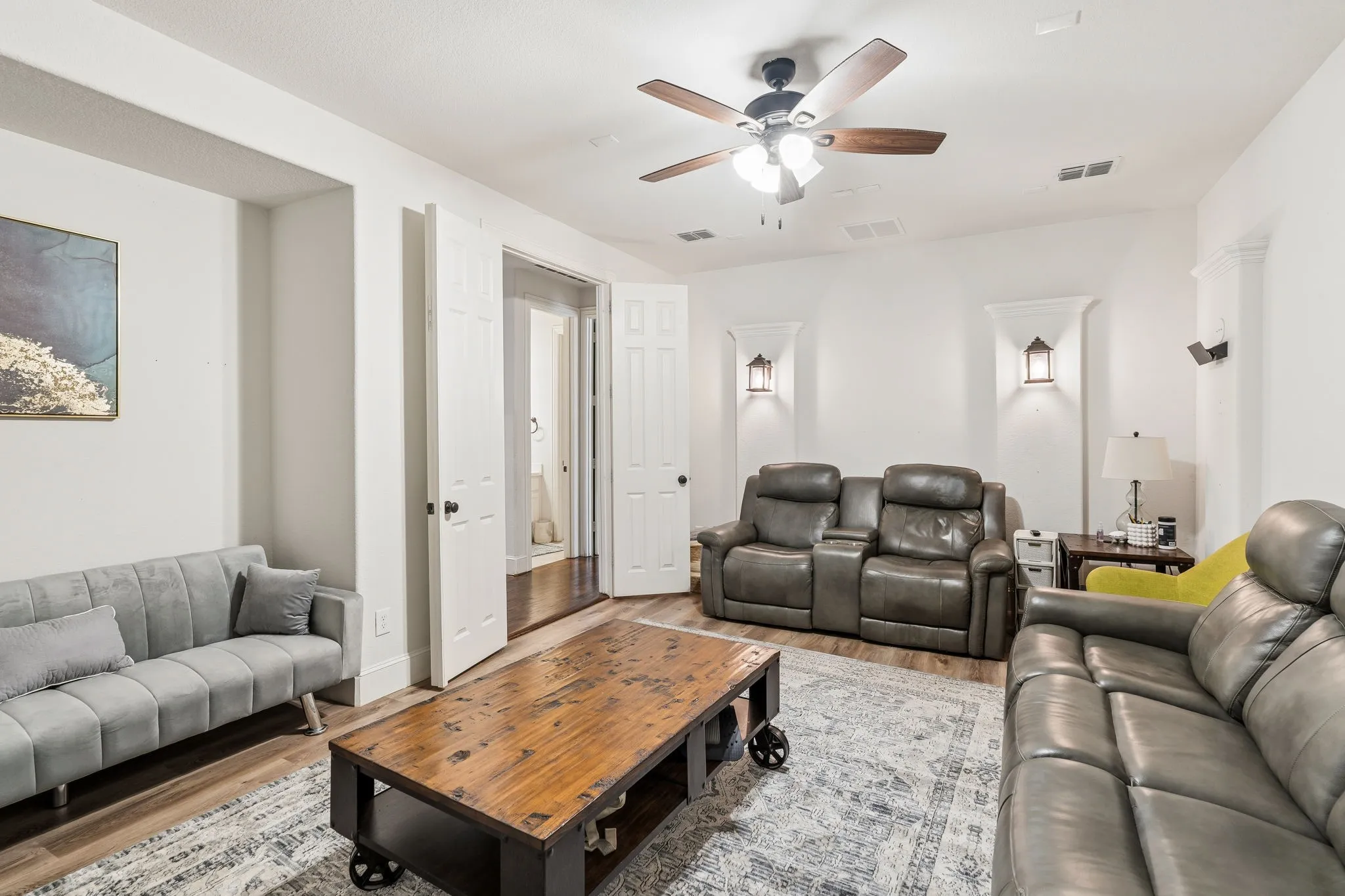 Open-concept living space featuring wood-finish flooring, a ceiling fan with integrated lighting, recessed lighting, and decorative wall sconces