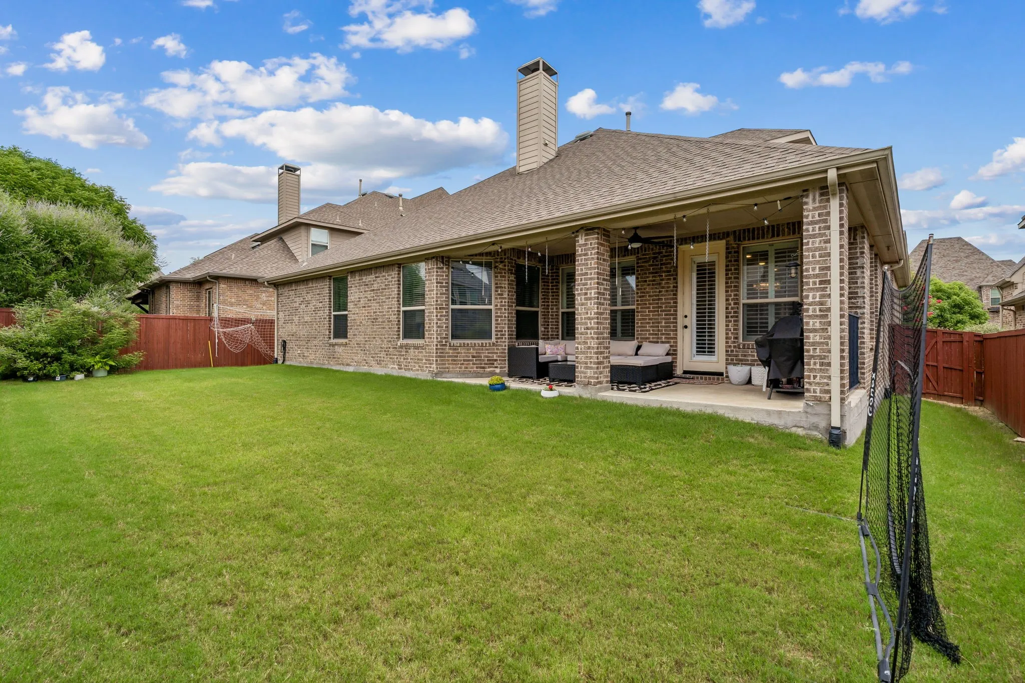 Spacious backyard featuring a covered patio with brick columns, a substantial grassy area, and perimeter fencing