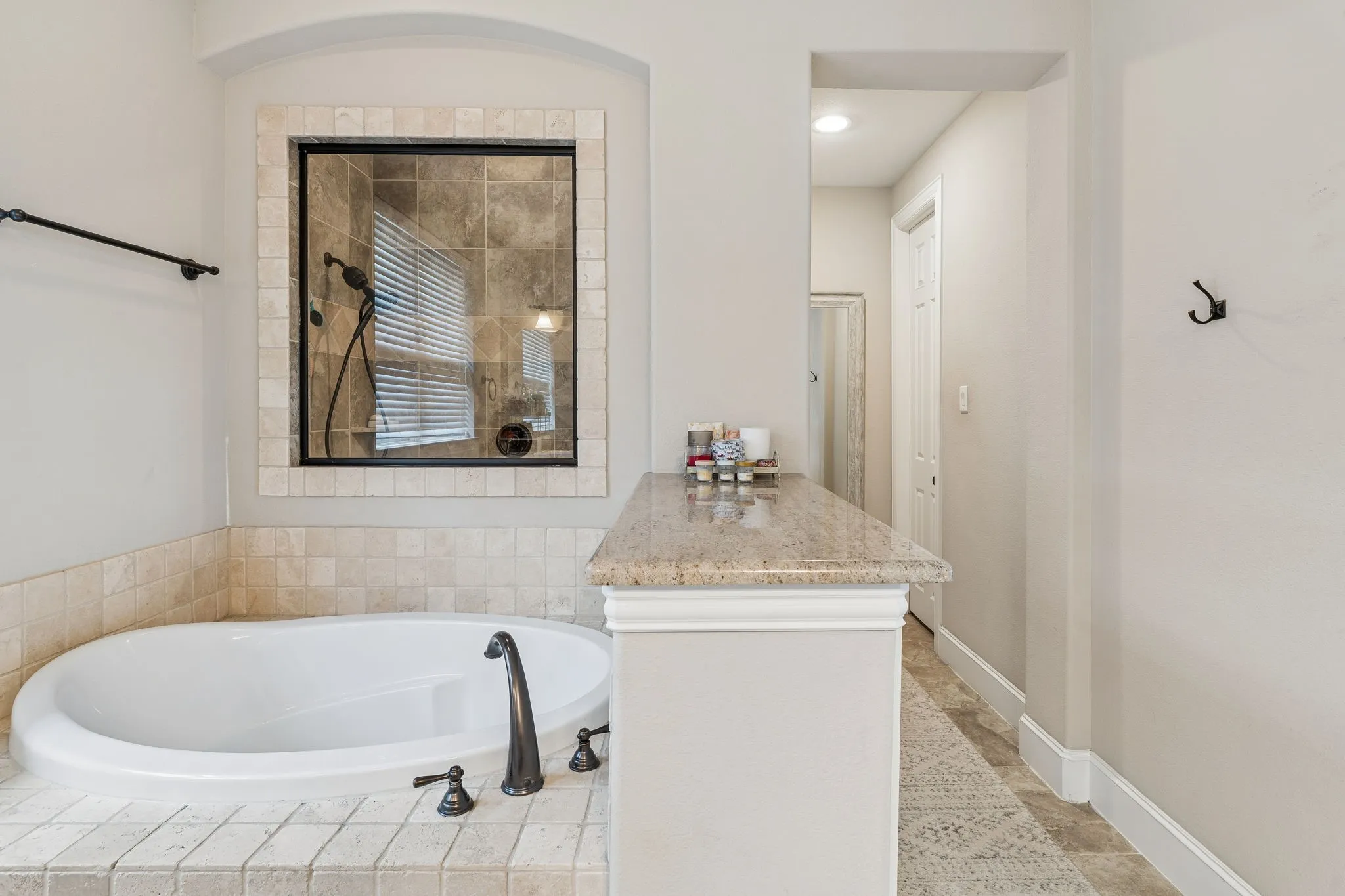 Soaking tub with bronze fixtures, surrounded by neutral-toned tilework