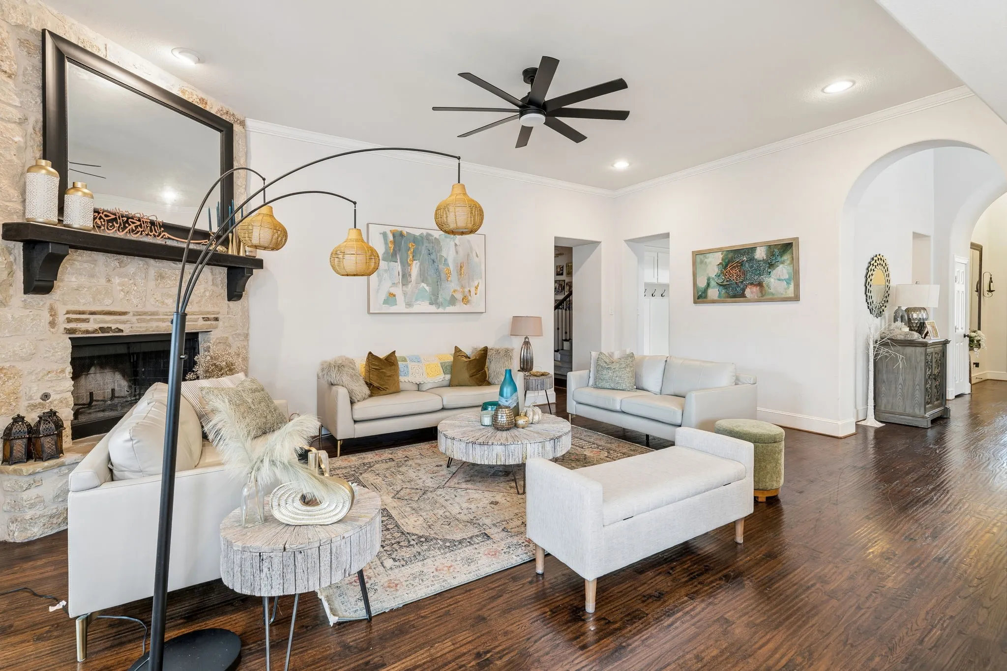 Spacious living room featuring a stone fireplace with a dark wood mantel, rich wood-finish flooring, recessed lighting, a ceiling fan, and arched doorways