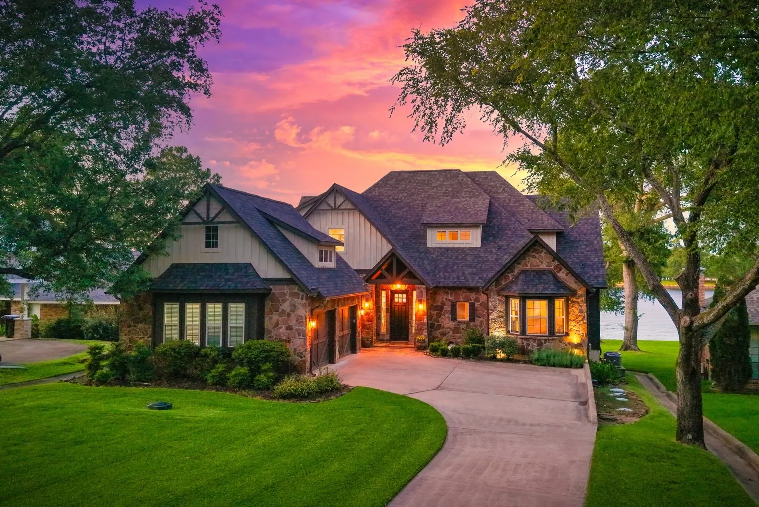 Hill Country style meets classic lakehouse charm in this waterfront home with a stone and wood exterior. Street side view showing the two car garage.