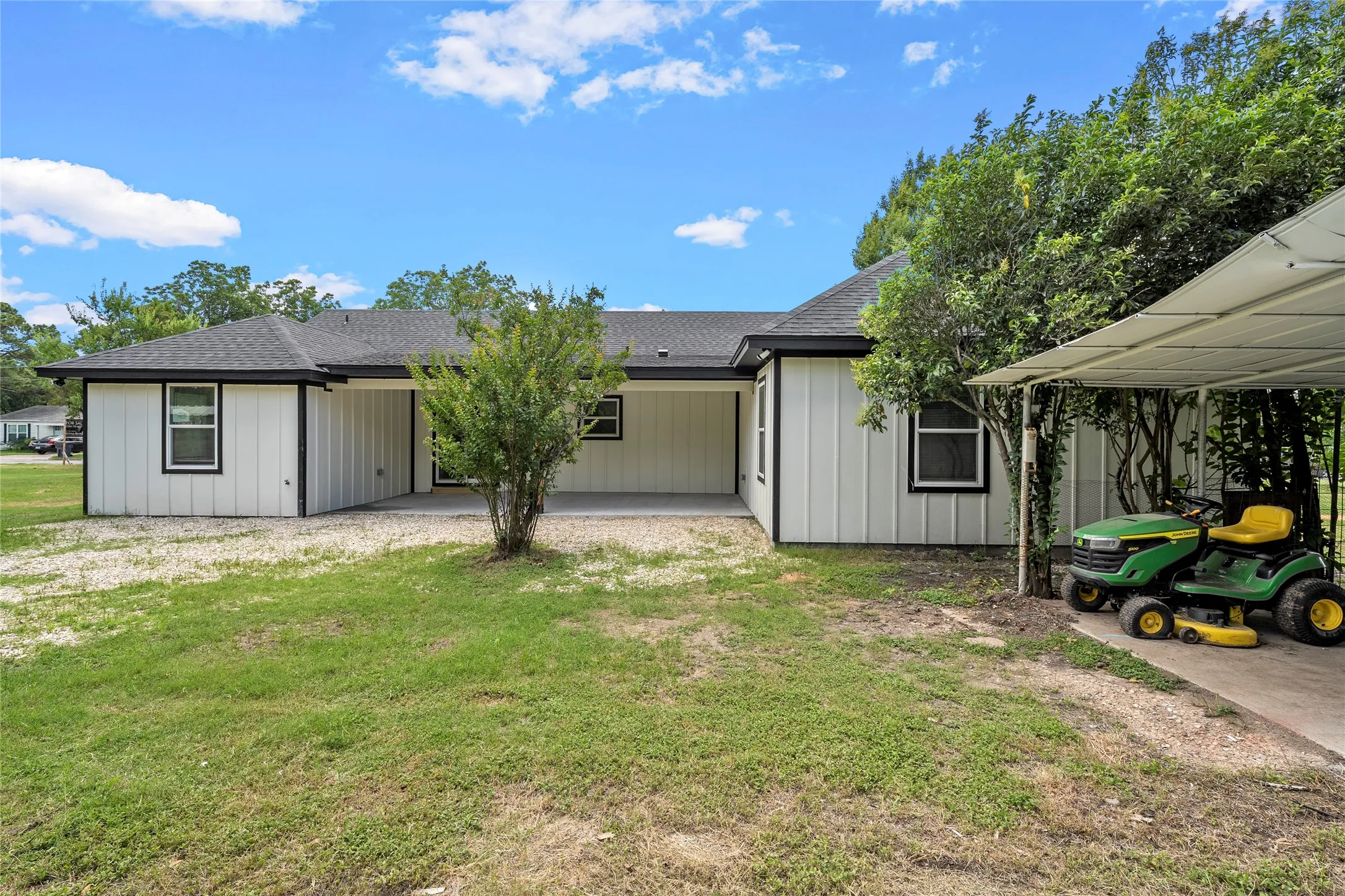 Rear exterior featuring white board and batten siding with black trim, a covered patio, and a covered carport structure
