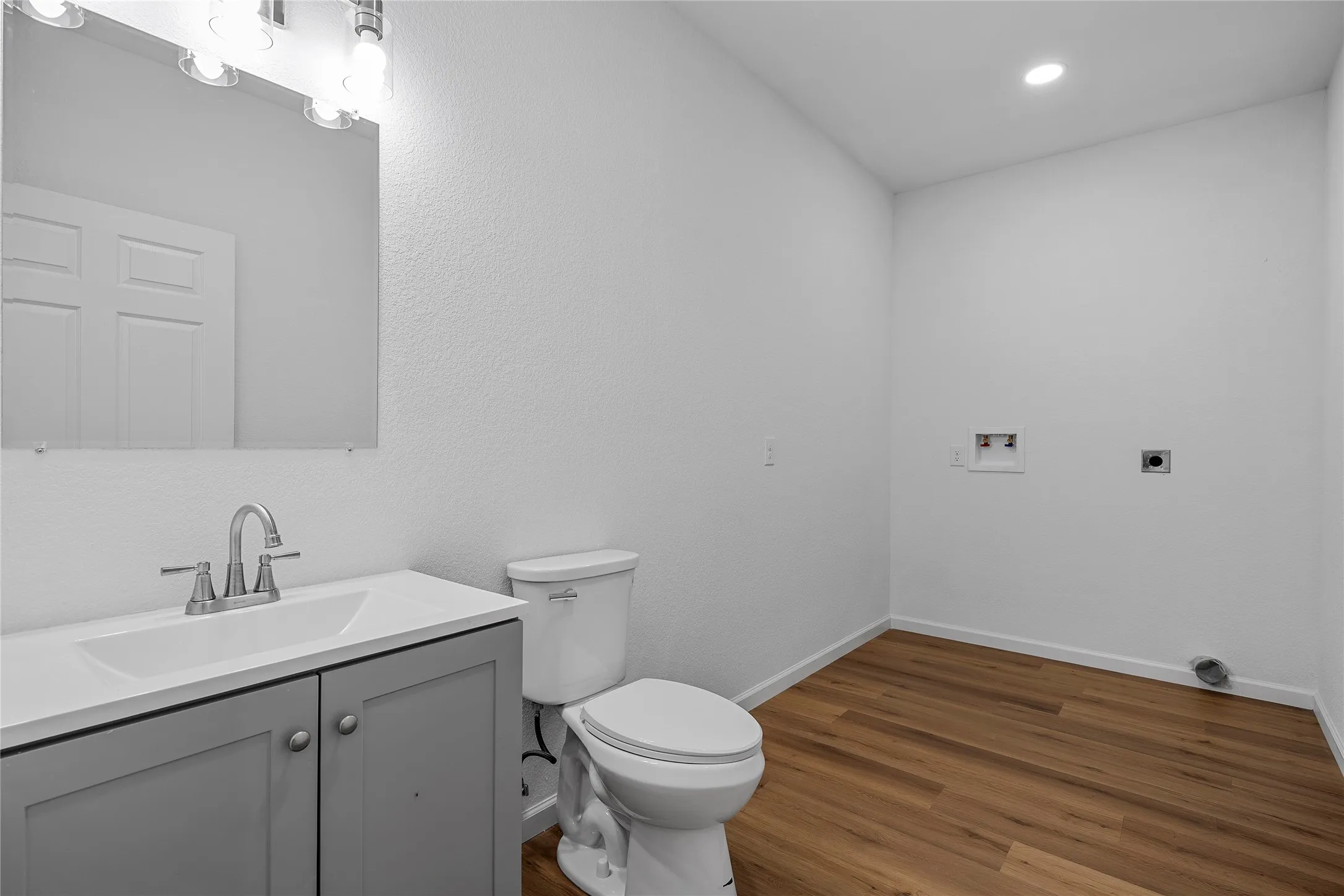 Light-filled utility room featuring wood-finish flooring, a contemporary vanity with an integrated sink, a sleek toilet, and dedicated laundry connections