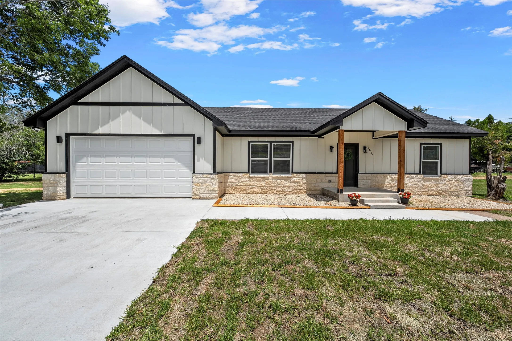 Contemporary single-story residence featuring white board and batten siding, stone veneer accents, a dark asphalt shingle roof, and a prominent two-car garage