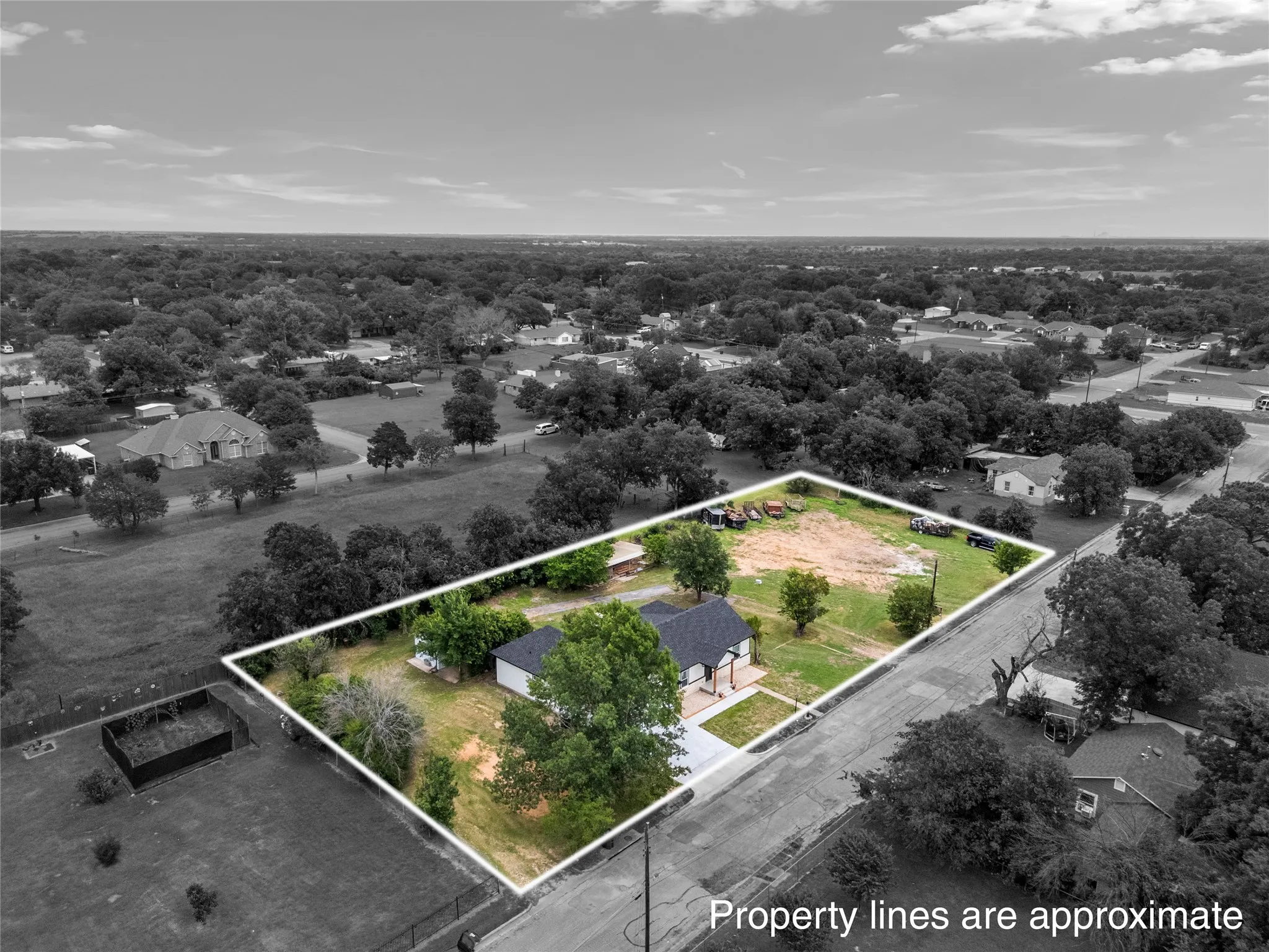 Expansive lot featuring a single-story residence with a dark roof and light exterior, mature trees, and undeveloped land