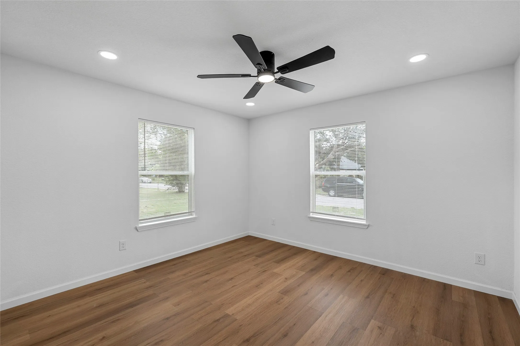 Room featuring wood-finish flooring, two windows, recessed lighting, and a ceiling fan with integrated light
