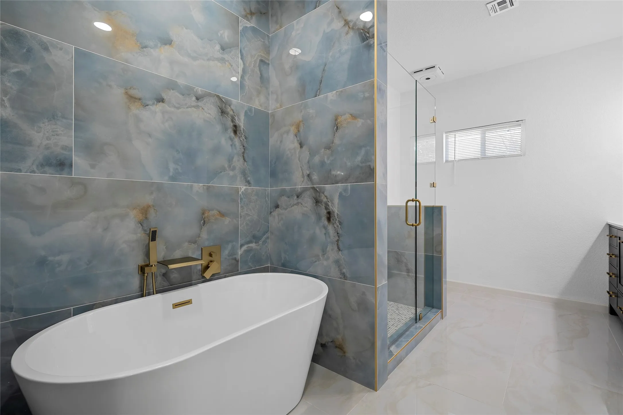 Freestanding soaking tub with gold-finish fixtures and blue-hued marbled wall tiling
