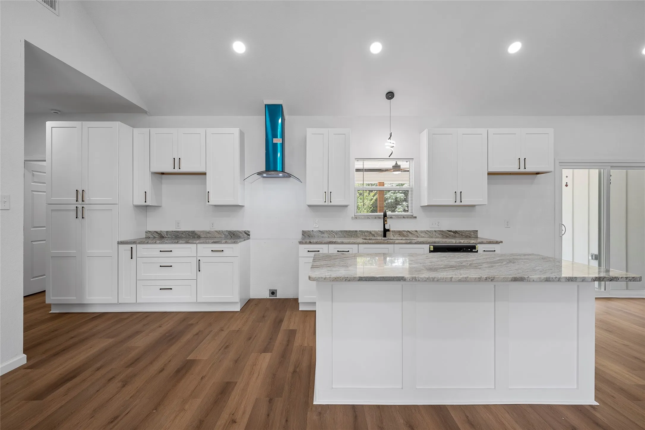 Modern kitchen featuring a central island with an extended counter, white shaker-style cabinetry, dark hardware, light-toned countertops, and wood-finish flooring