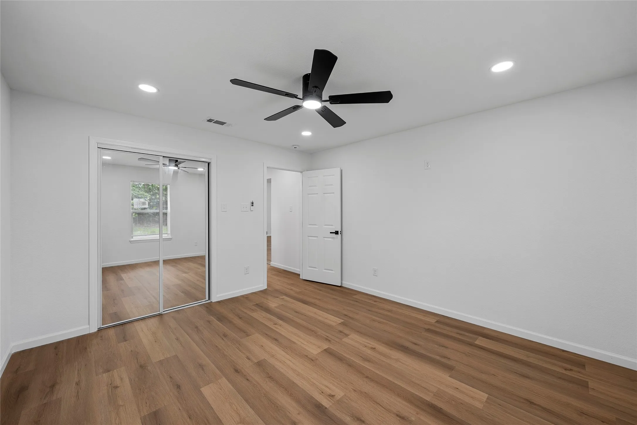 Spacious room featuring wood-finish flooring, a contemporary ceiling fan, recessed lighting, and mirrored closet doors