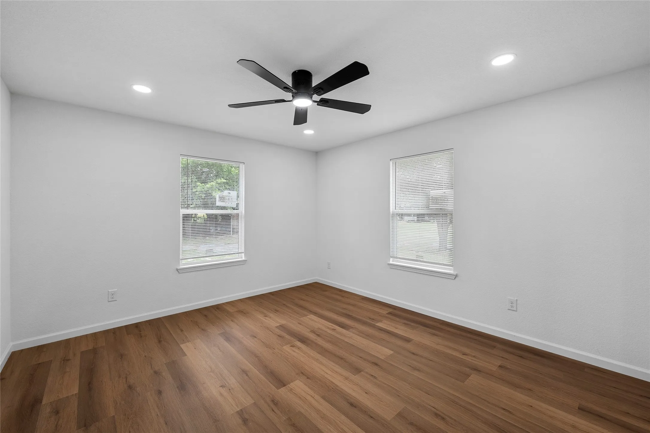Room featuring wood-finish flooring, two windows, recessed lighting, and a ceiling fan with integrated lighting