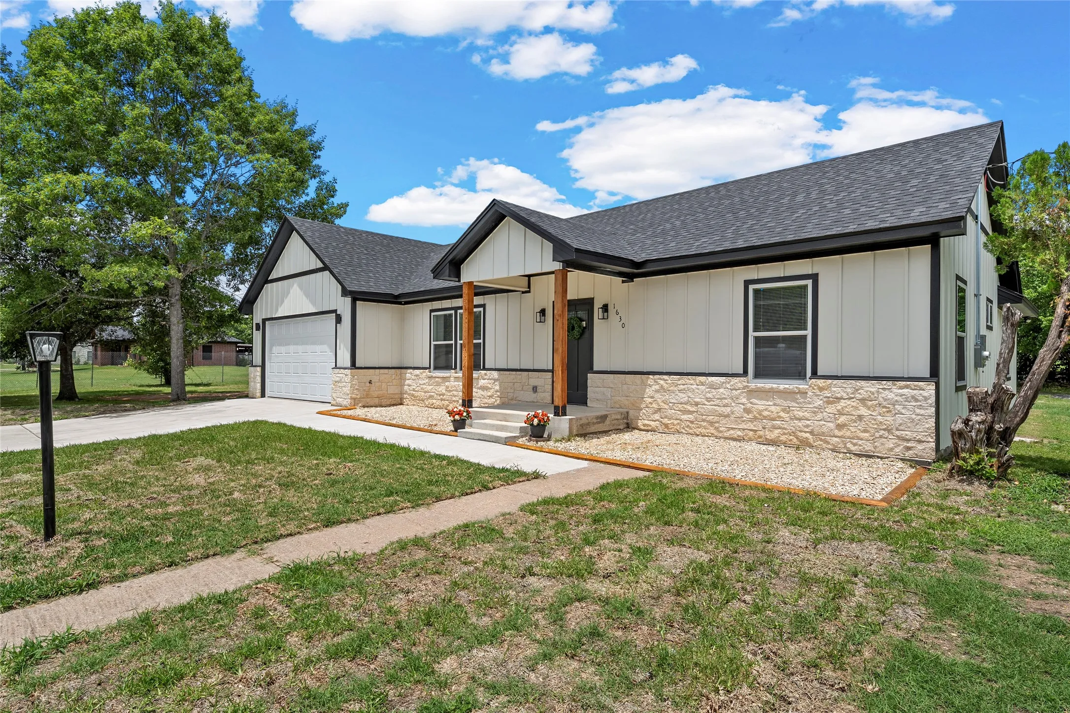 Contemporary exterior featuring white board and batten siding, a stone veneer foundation, and a dark shingle roof