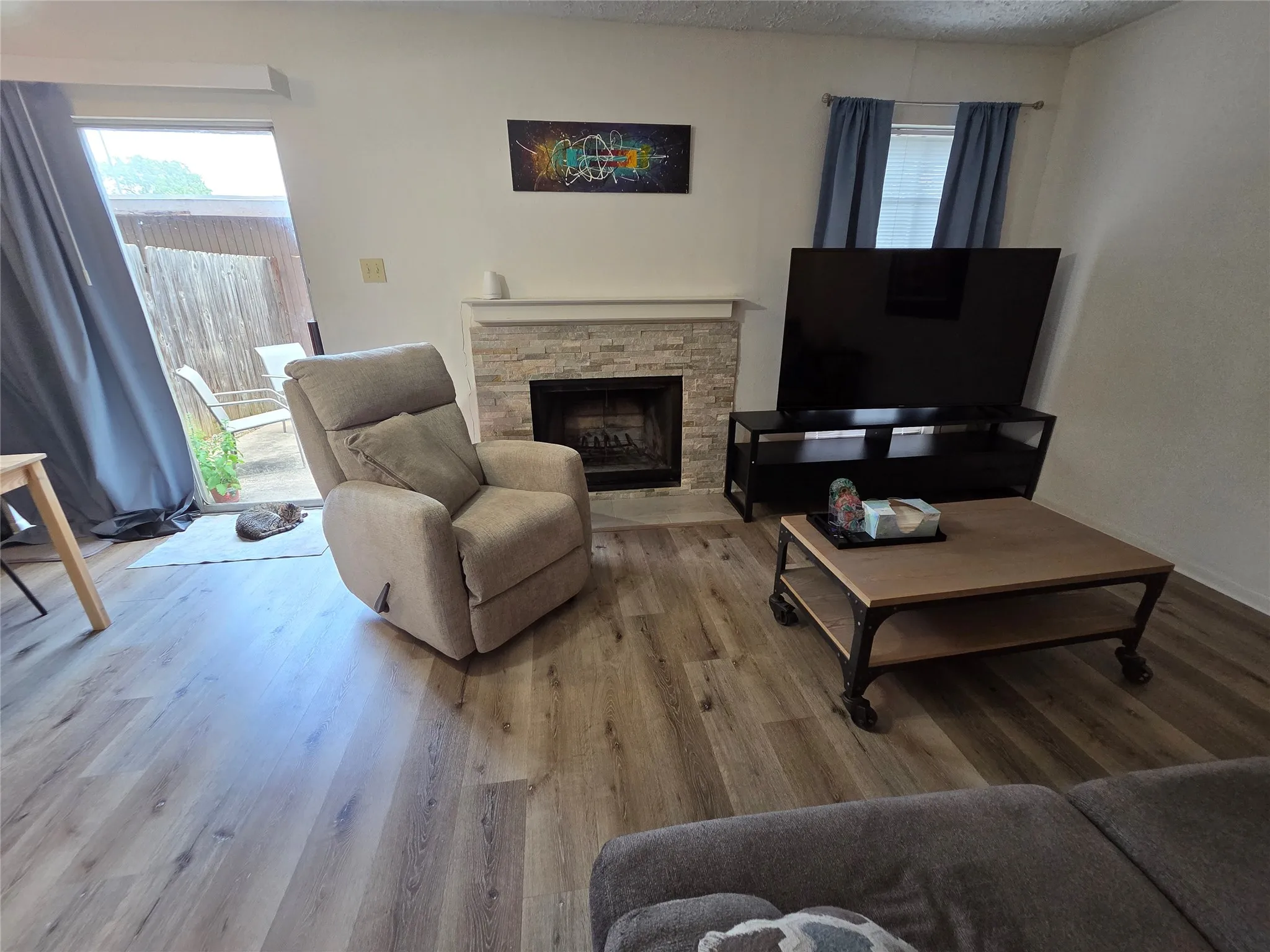 Living area with wood-finish flooring, a stone-clad fireplace, and sliding glass door access to an outdoor space