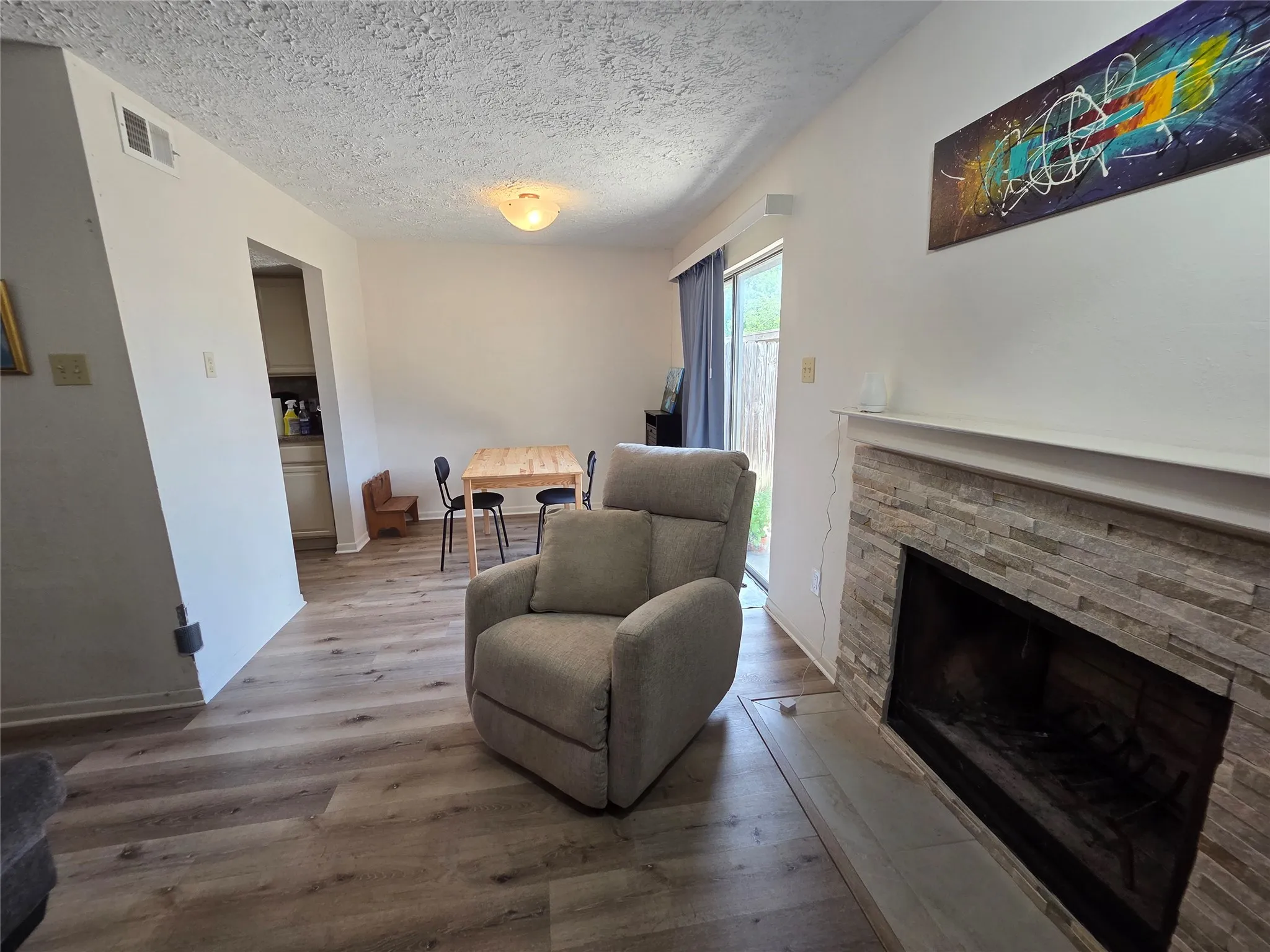 Living area with wood-finish flooring, a stone-faced fireplace, and a white mantel