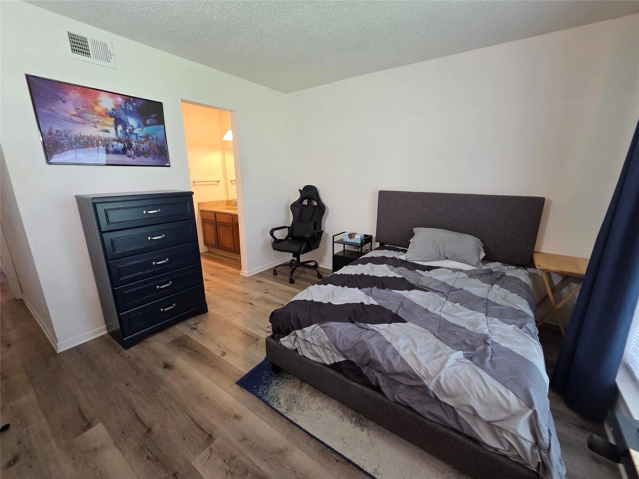 Room featuring wood-finish flooring, white painted walls, and a visible doorway to a bathroom with a wood-finish vanity