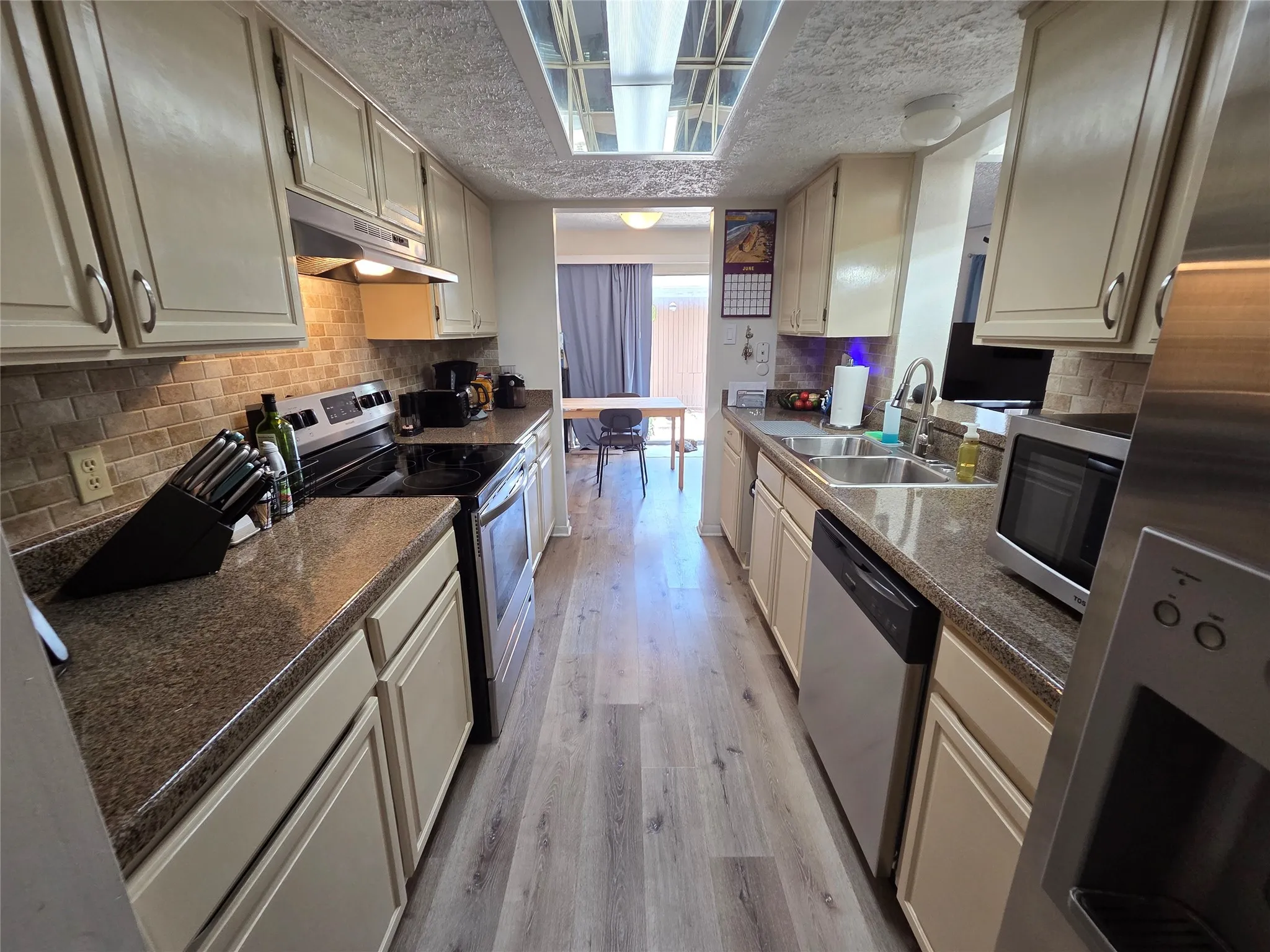 Galley kitchen featuring light wood-finish flooring, light-toned cabinetry, and dark countertops