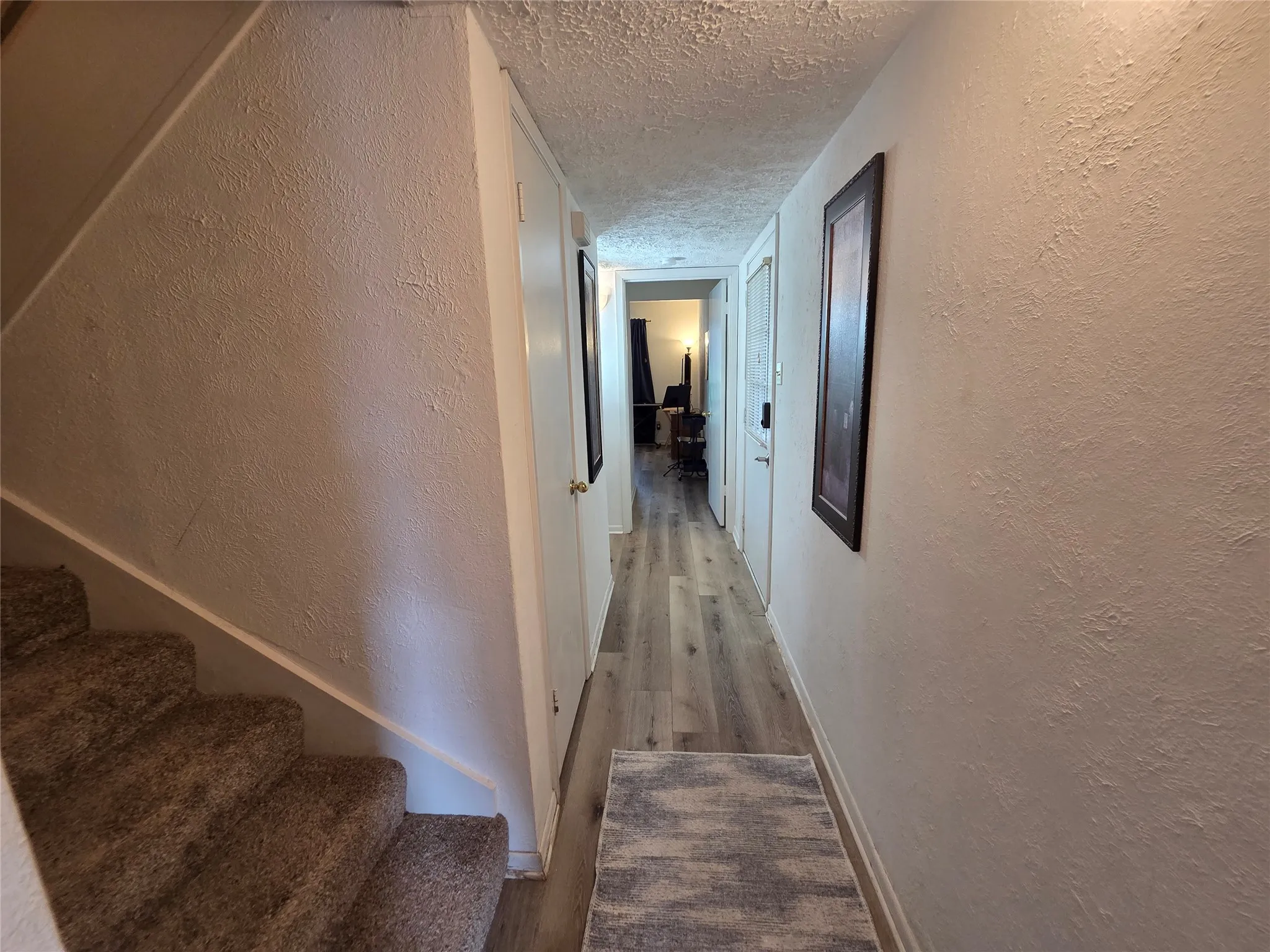 Hallway featuring wood-finish flooring, white doors, and a carpeted staircase