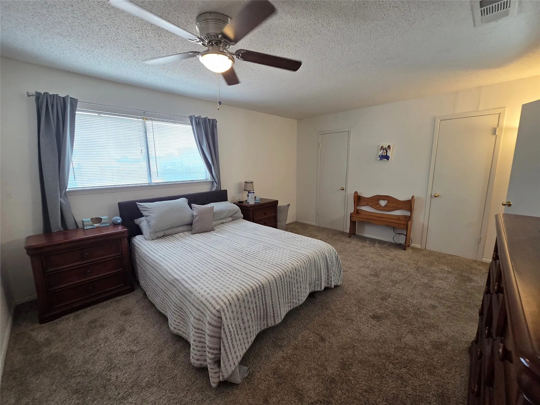 Spacious bedroom featuring neutral wall paint, two windows with blinds, a ceiling fan with integrated lighting, and plush carpeting