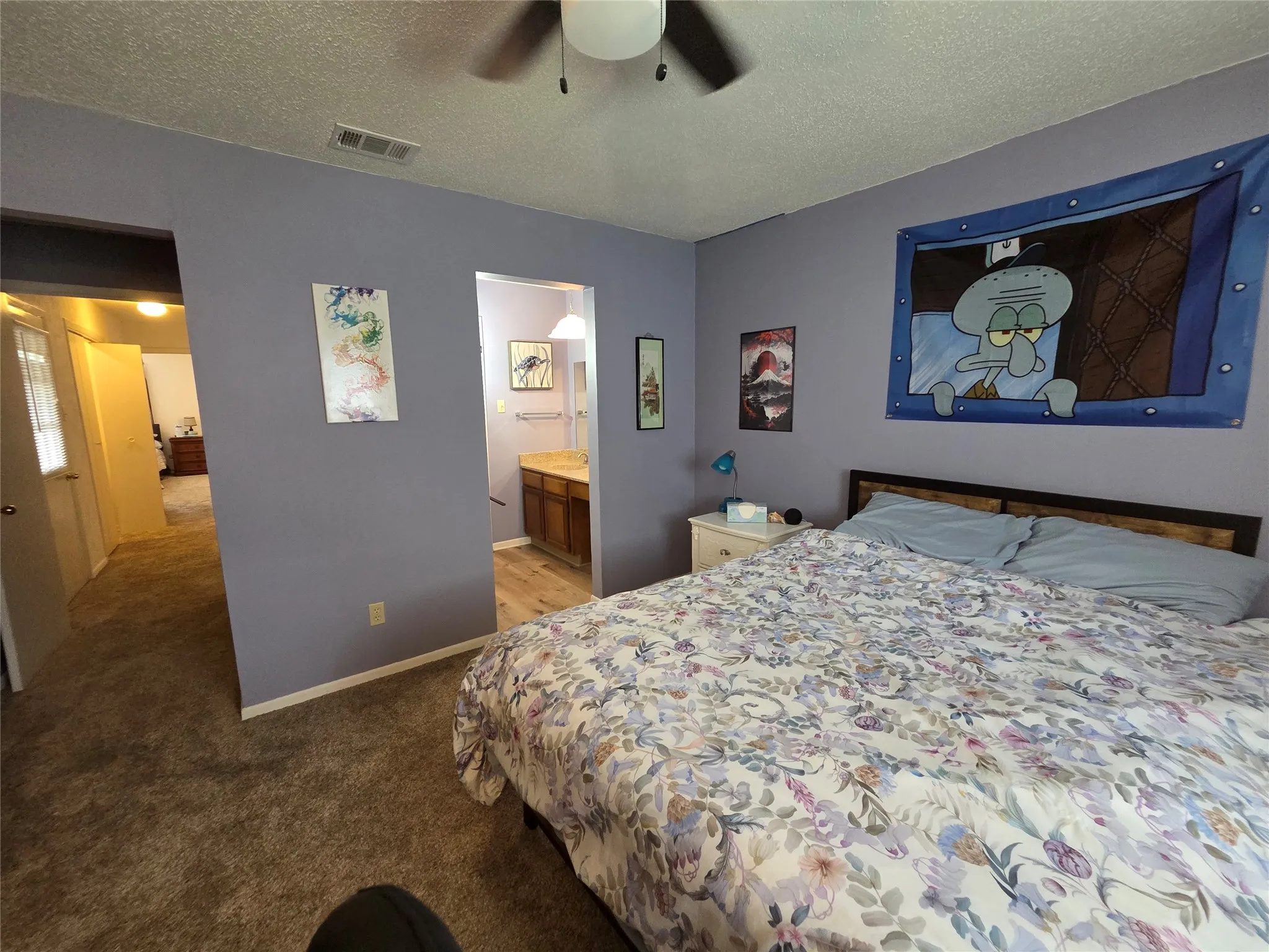 Bedroom featuring plush carpet flooring, a ceiling fan, and direct access to a bathroom with wood-finish cabinetry