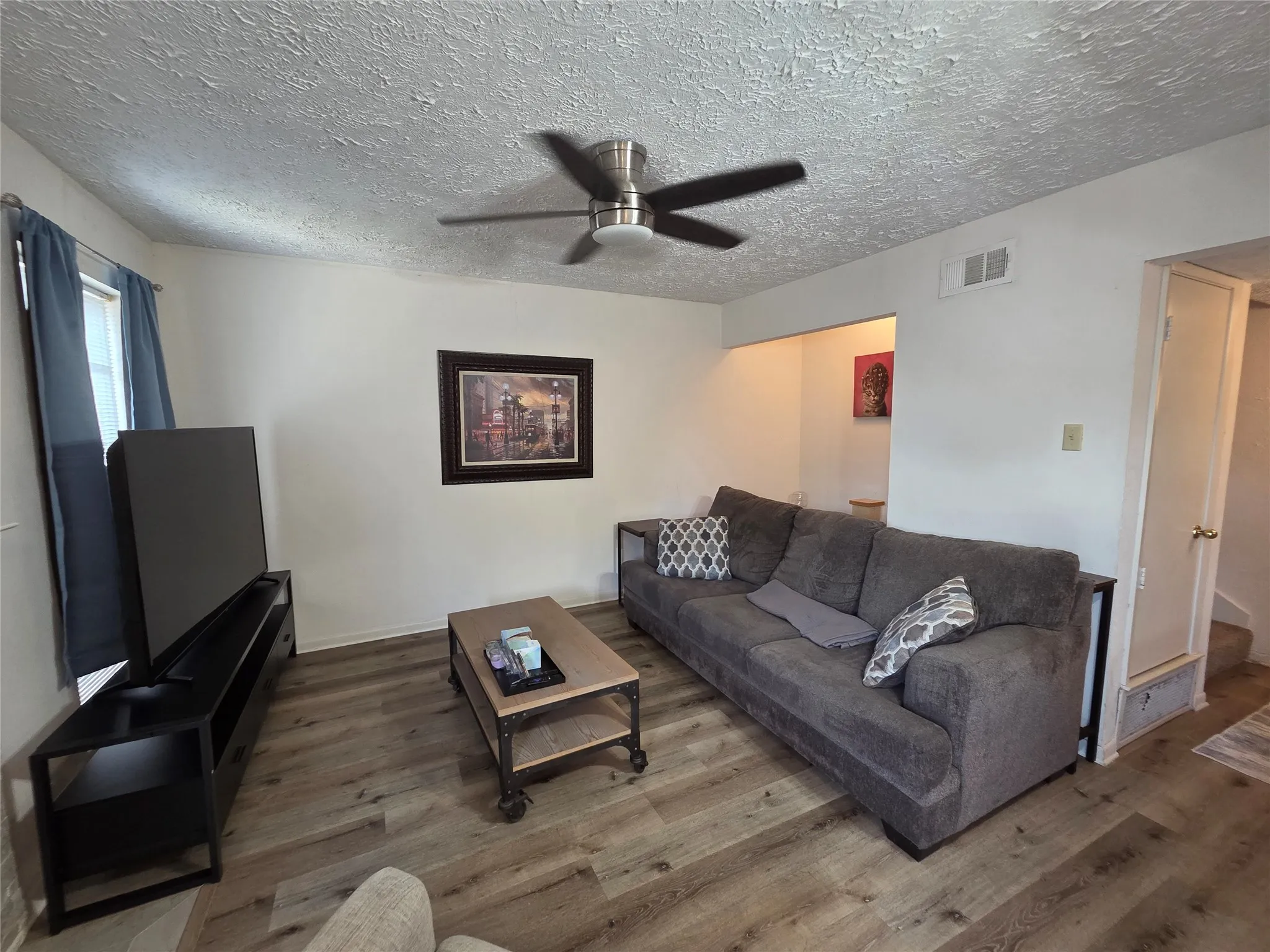 Living area featuring wood-finish flooring, white walls, and a ceiling fan with brushed nickel accents