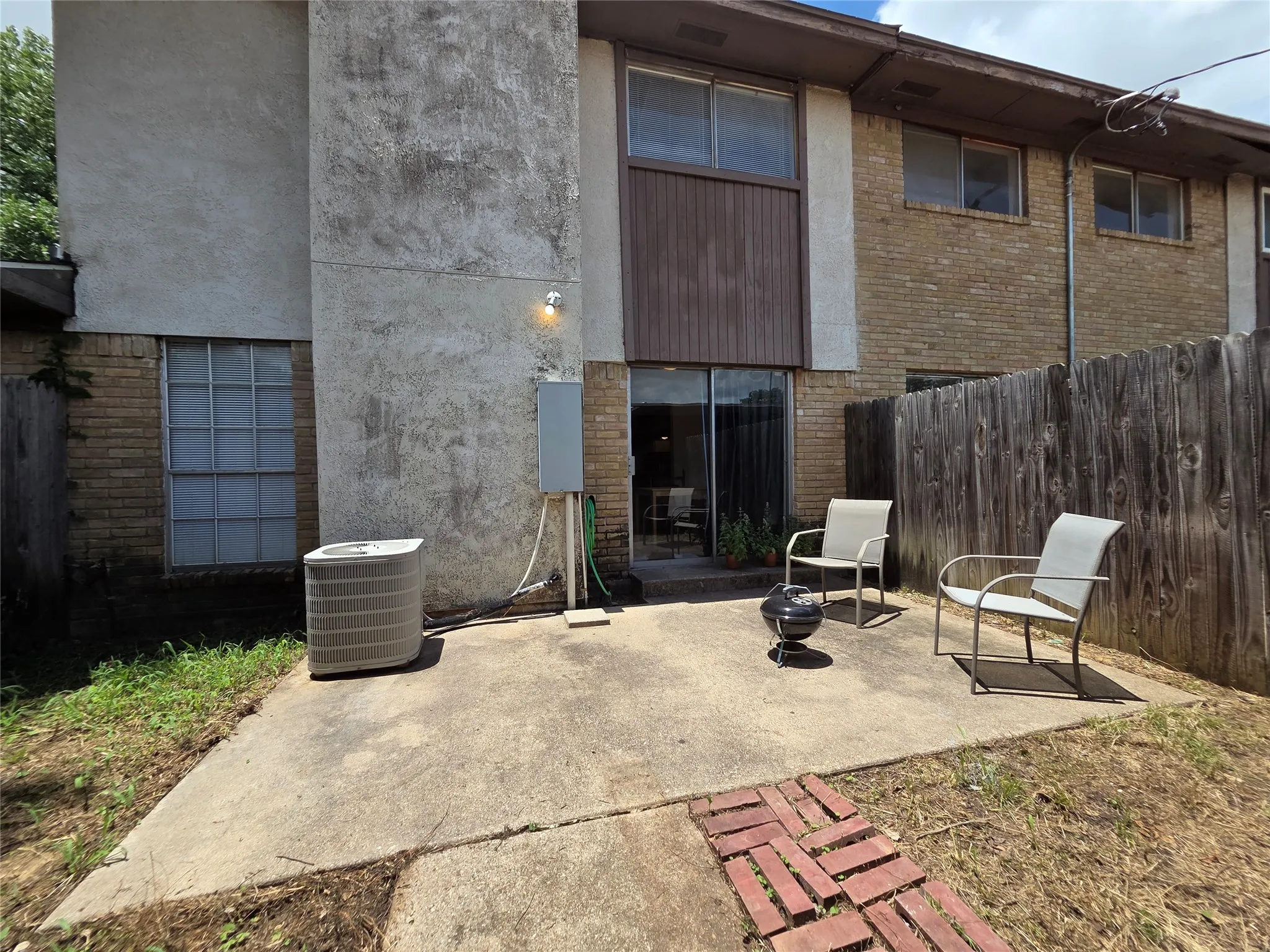 Concrete patio area featuring a sliding glass door entry, exterior wall sconce, and a partial brick facade